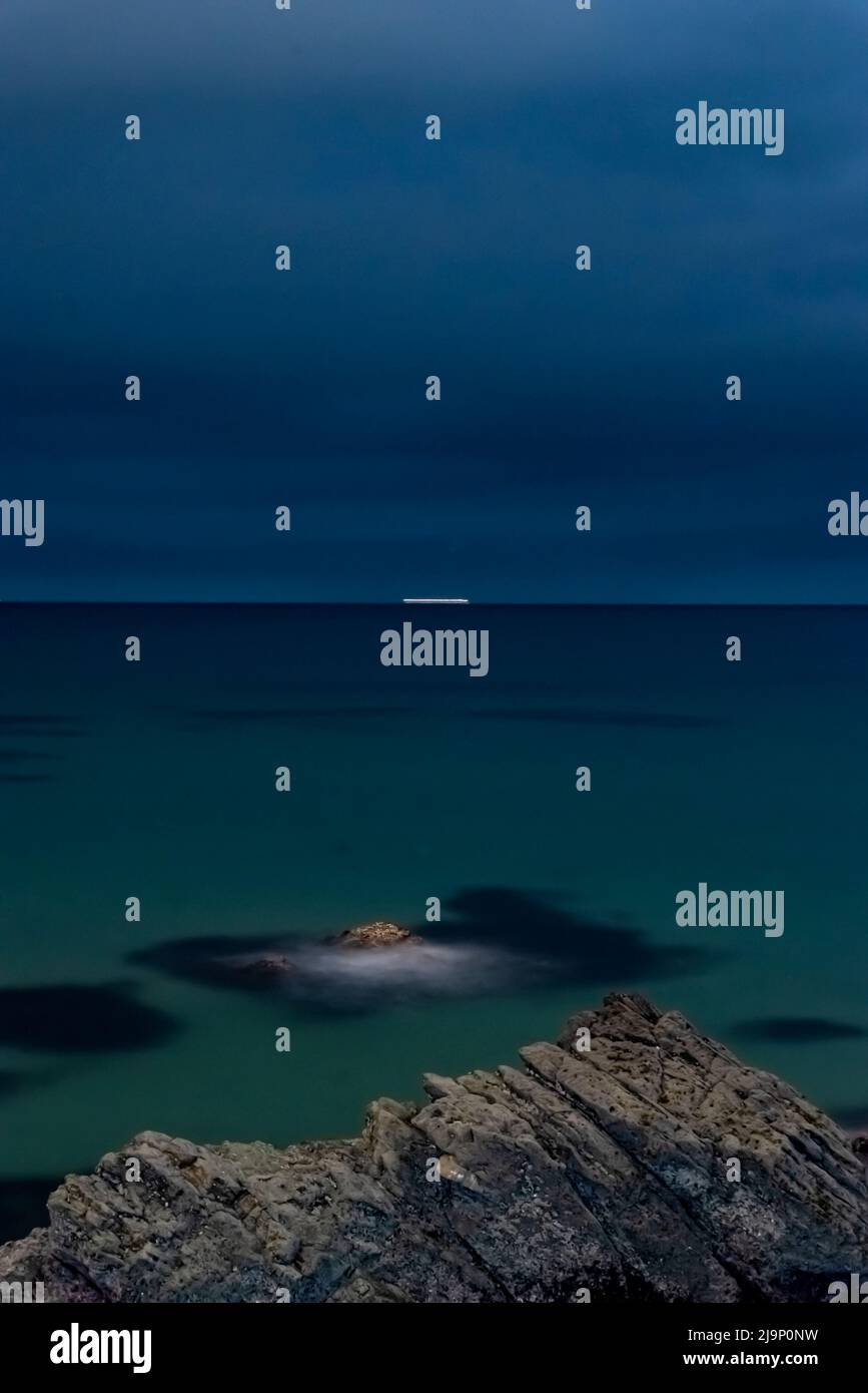 Lange Belichtungszeit in der Nacht Seestücke auf Kamera mit Felsen im Vordergrund ein wenig höher und seidigen Schatten am Horizont, wolkigen Himmel Nachtbild Stockfoto