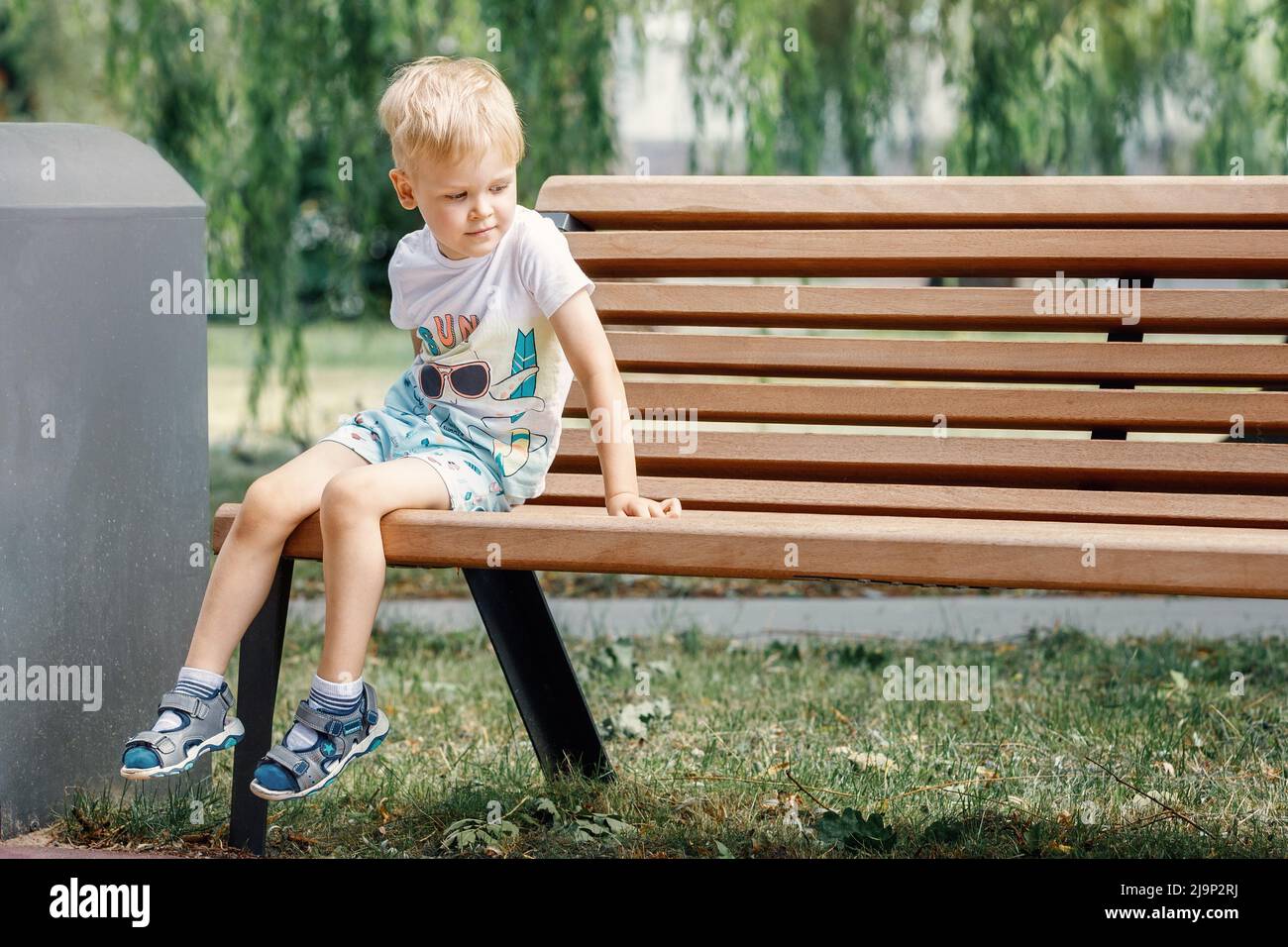 Kleines Kind spielt im Park, klettert auf die Bank. Das Kind sitzt auf einer Parkbank. Stockfoto