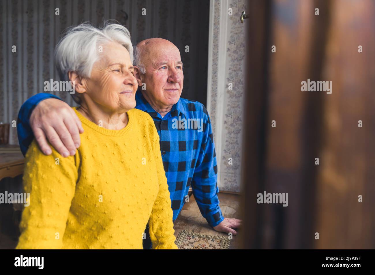Nettes älteres kaukasisches Paar mit Blick aus dem Fenster und lächelndem Mittelschuss-Konzept im Innenbereich. Hochwertige Fotos Stockfoto