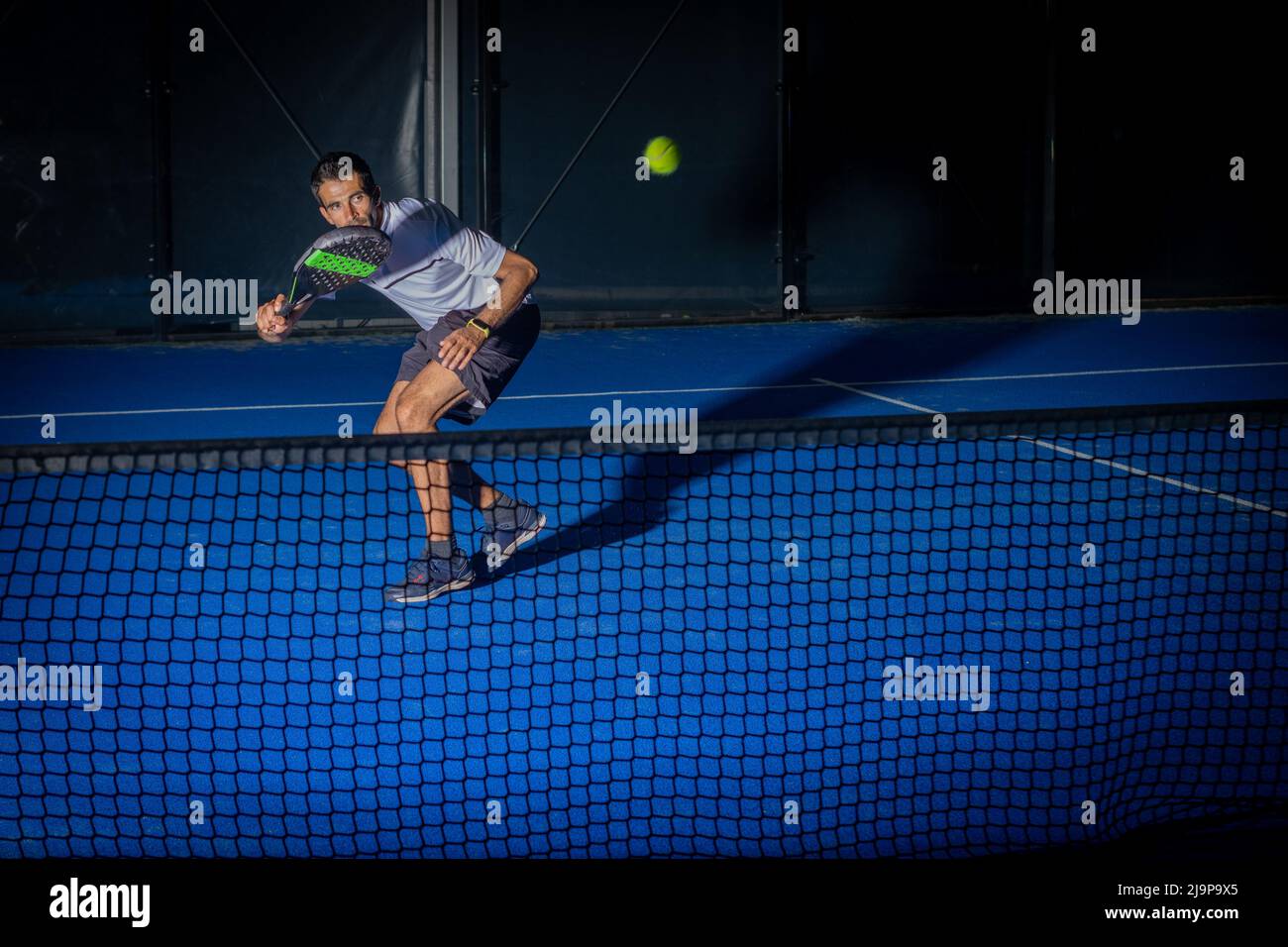 Sportlicher europäischer Mann in weißem T-Shirt, der in der Halle Padel Tennis spielt Stockfoto