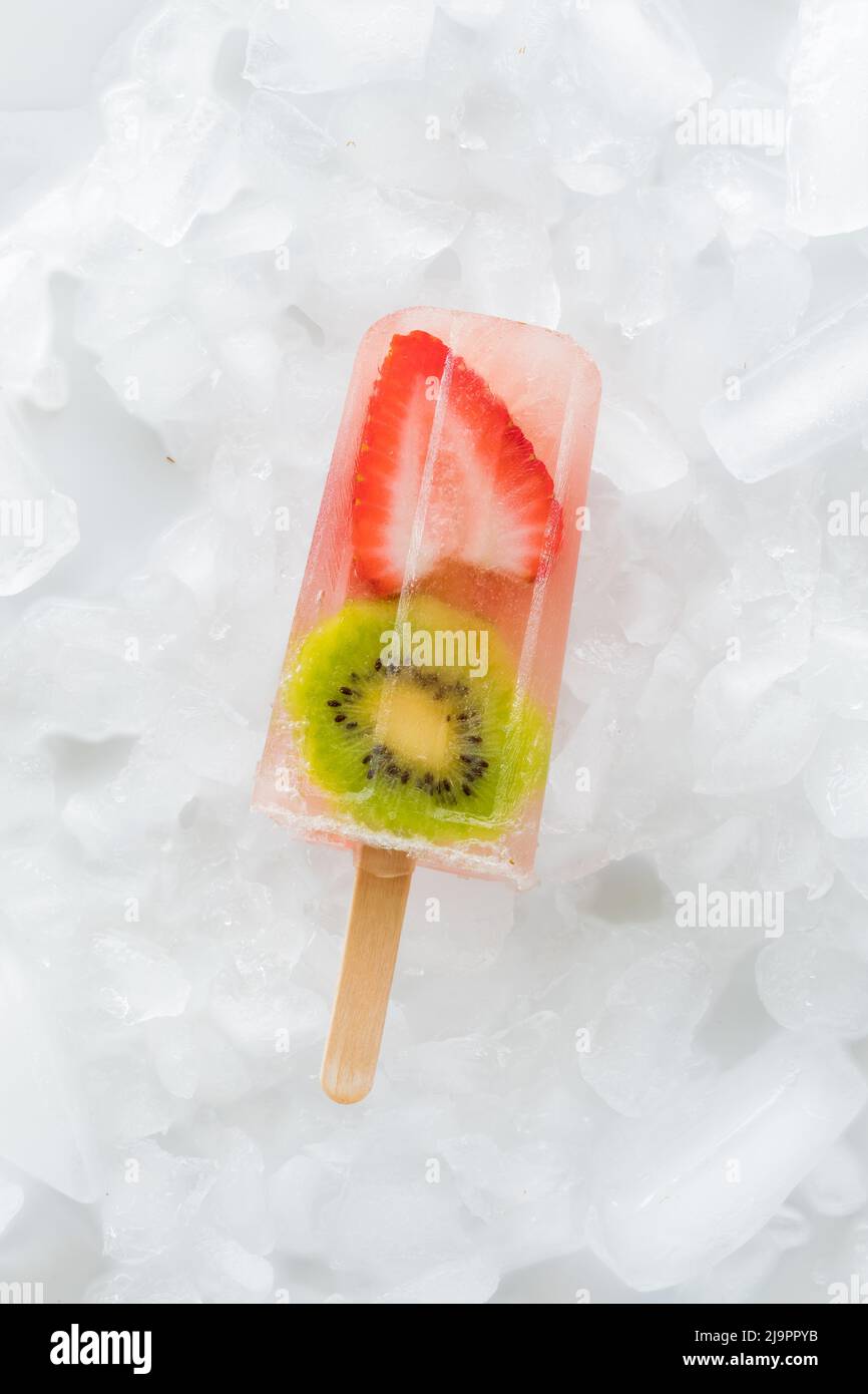 Eine einzelne Erdbeer-Kiwi-Popsicles, isoliert auf einem Eisbett. Stockfoto
