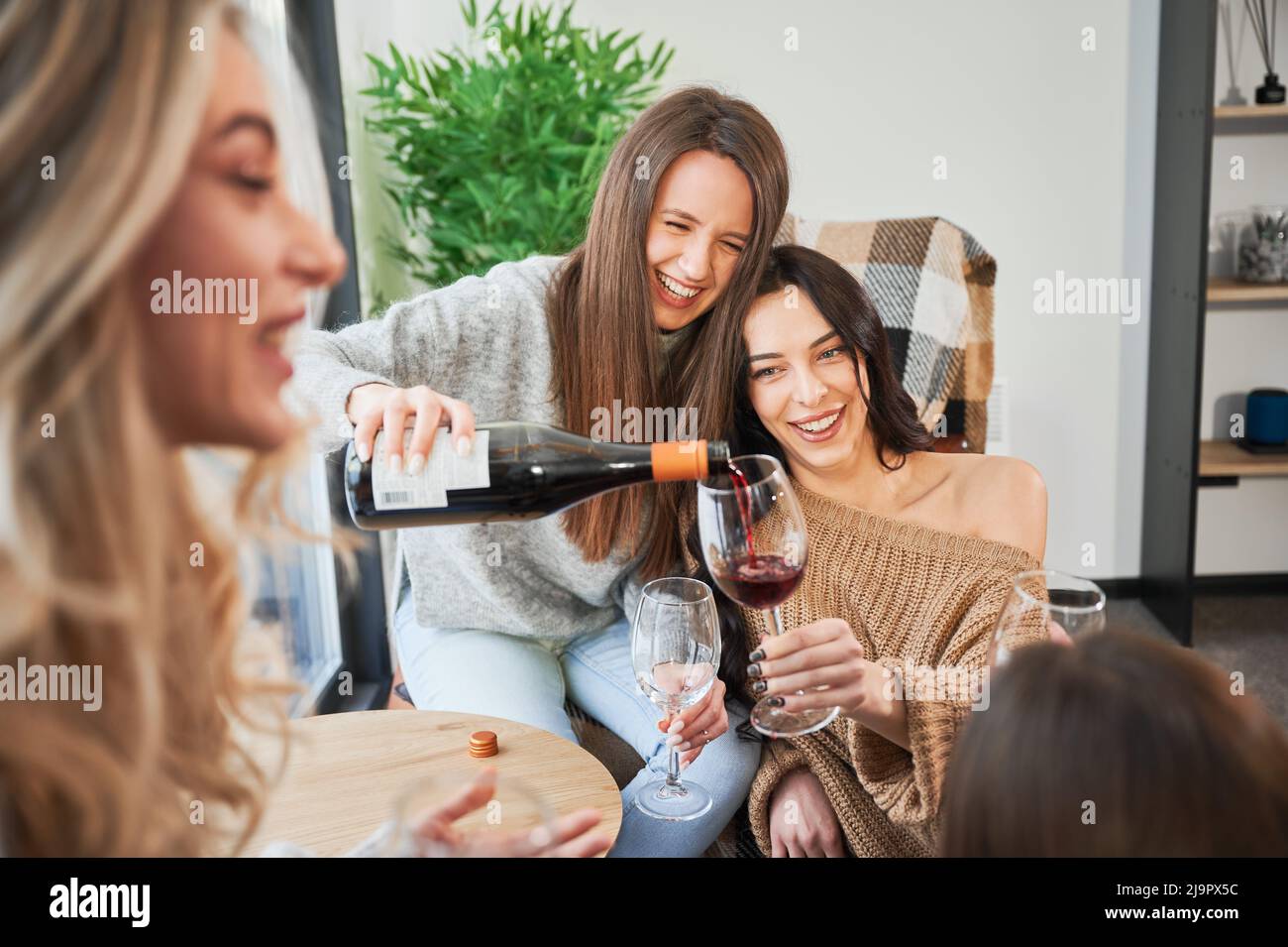 Junge Frauen genießen Winterwochenenden im modernen Scheunenhaus. Vier Mädchen, die Spaß haben und Wein trinken. Stockfoto