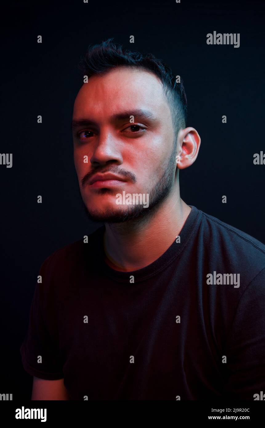 Latino Mann posiert mit blauen und roten Lichtern auf schwarzem Hintergrund. Porträt eines weißen Mannes mit Neonlicht. Vertikales Selbstporträt Stockfoto