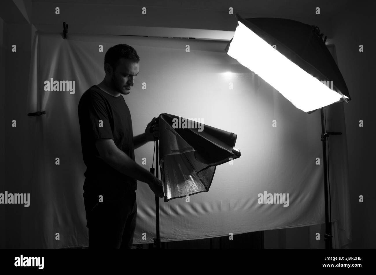 Der Mann bereitet sein Fotostudio vor. Der Fotograf passt die Studioleuchten an. Schwarzweißfoto des Fotografen bei der Arbeit. Stockfoto