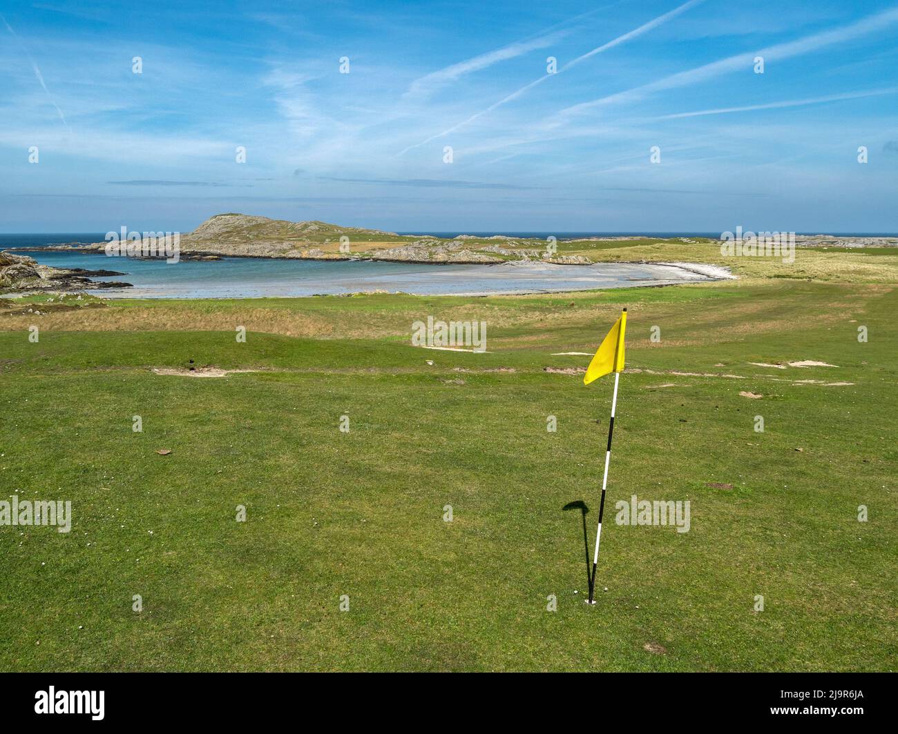 Grün mit Flagge auf dem küstennahen Machrins Golfplatz mit sandigen Port Lobh Strand dahinter auf der abgelegenen hebridischen schottischen Insel Colonsay, Schottland. Stockfoto