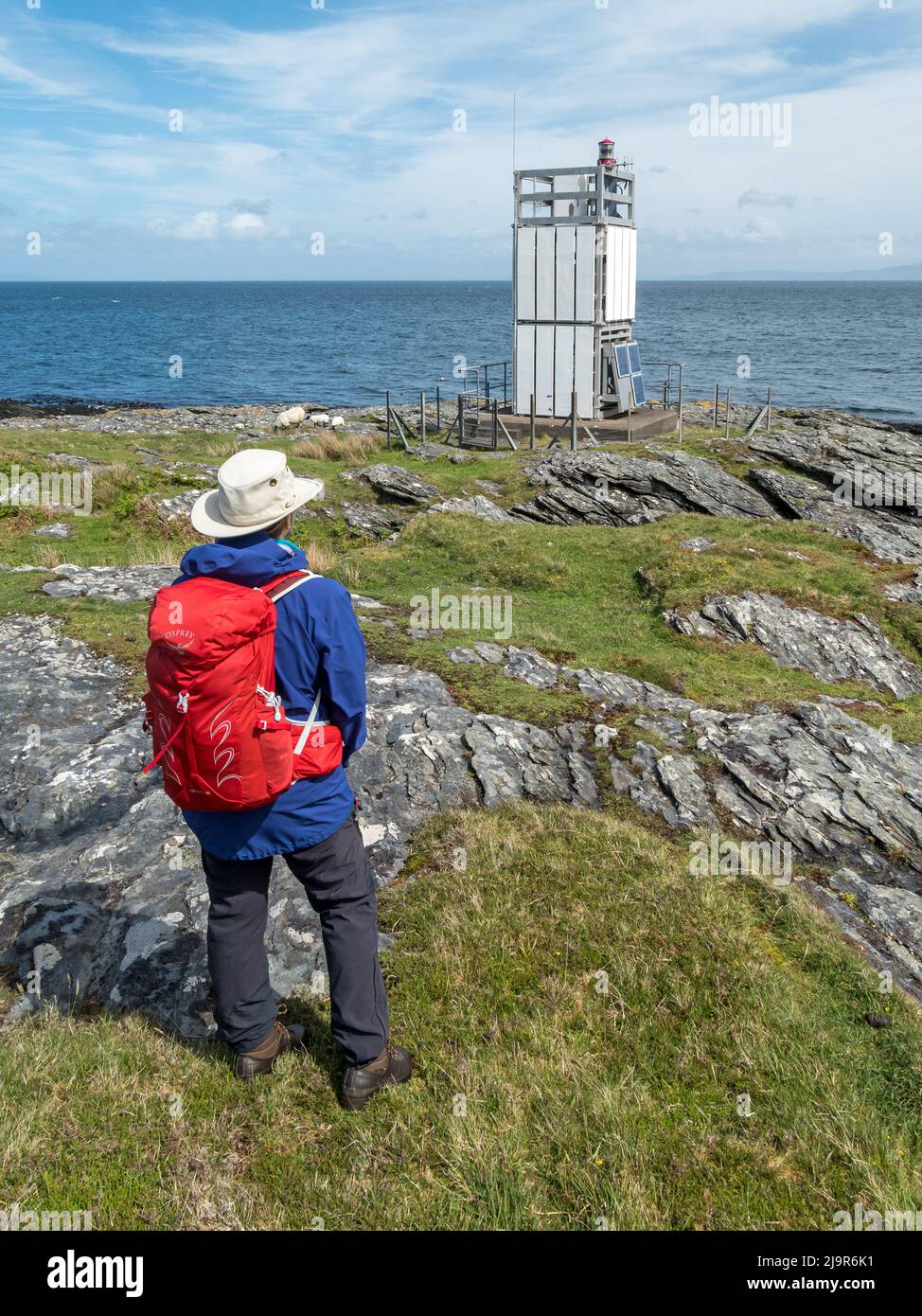Weibliche Wanderer mit Blick auf das Meer und den modernen, kleinen, unbemannten solarbetriebenen Leuchtturm in Scalasaig auf der Insel Colonsay, Schottland, Großbritannien Stockfoto