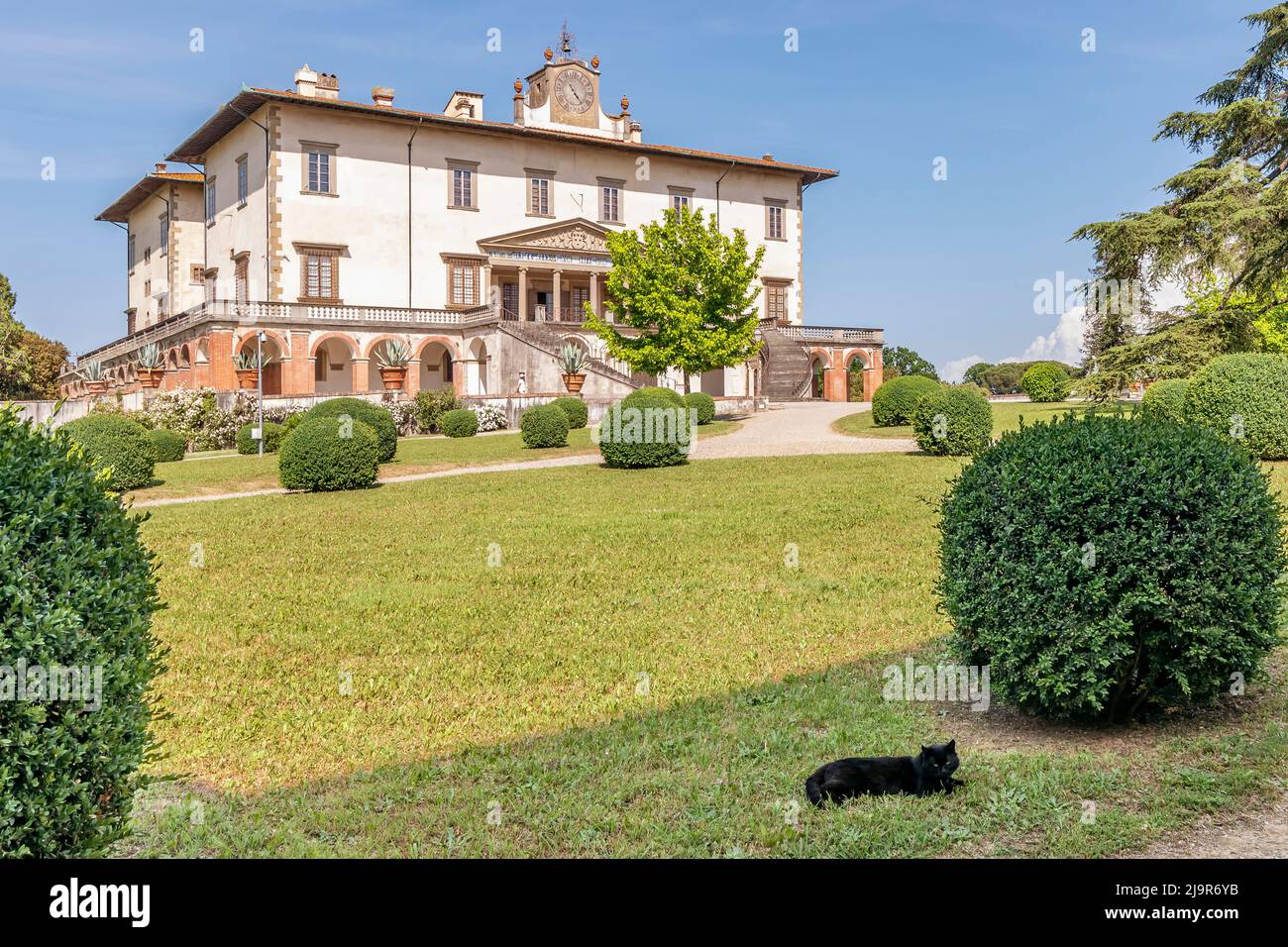 Eine schwarze Katze auf dem Gras mit der Medici-Villa von Poggio a Caiano im Hintergrund, Prato, Italien Stockfoto