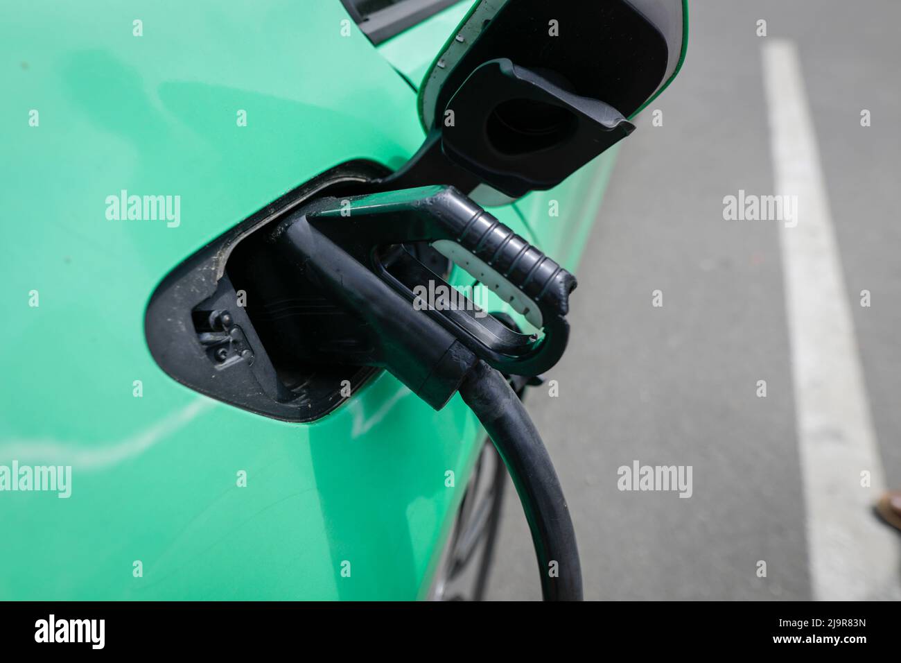 Shallow depth of field (selective focus) details with auto electric plug or socket at an electric vehicle charging station. Stockfoto