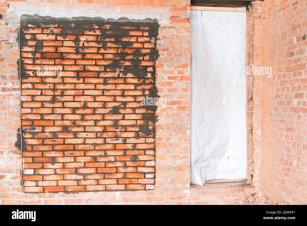 Der geheime Raum in der Wand ist zugemauert. Bunker in einem privaten Haus. Frisch verlegte rote Keramikmauer Stockfoto