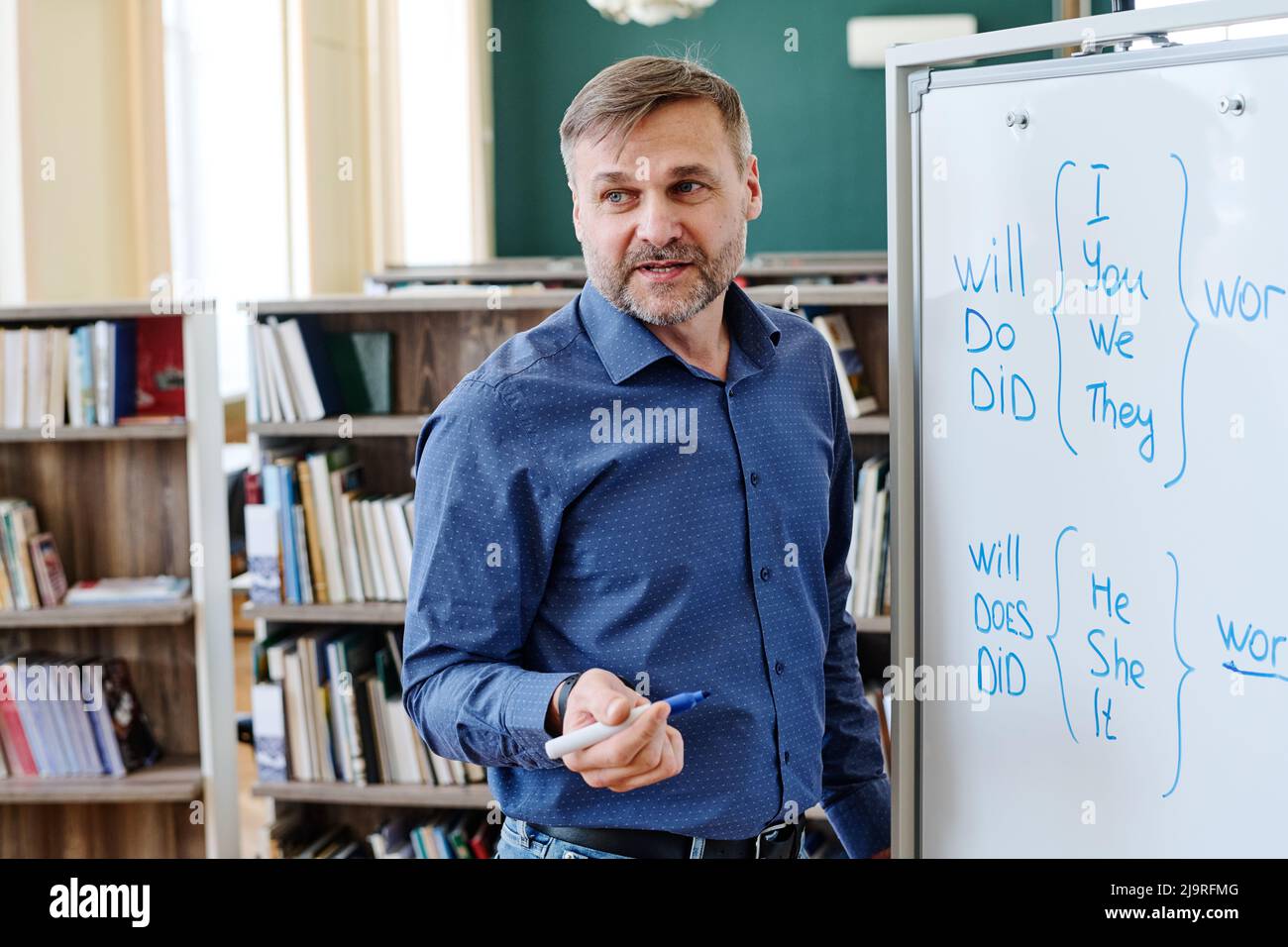 Porträt eines kaukasischen Mannes, der in der Schule arbeitet und am Whiteboard steht und seinen Schülern die englischen Grammatikregeln erklärt Stockfoto