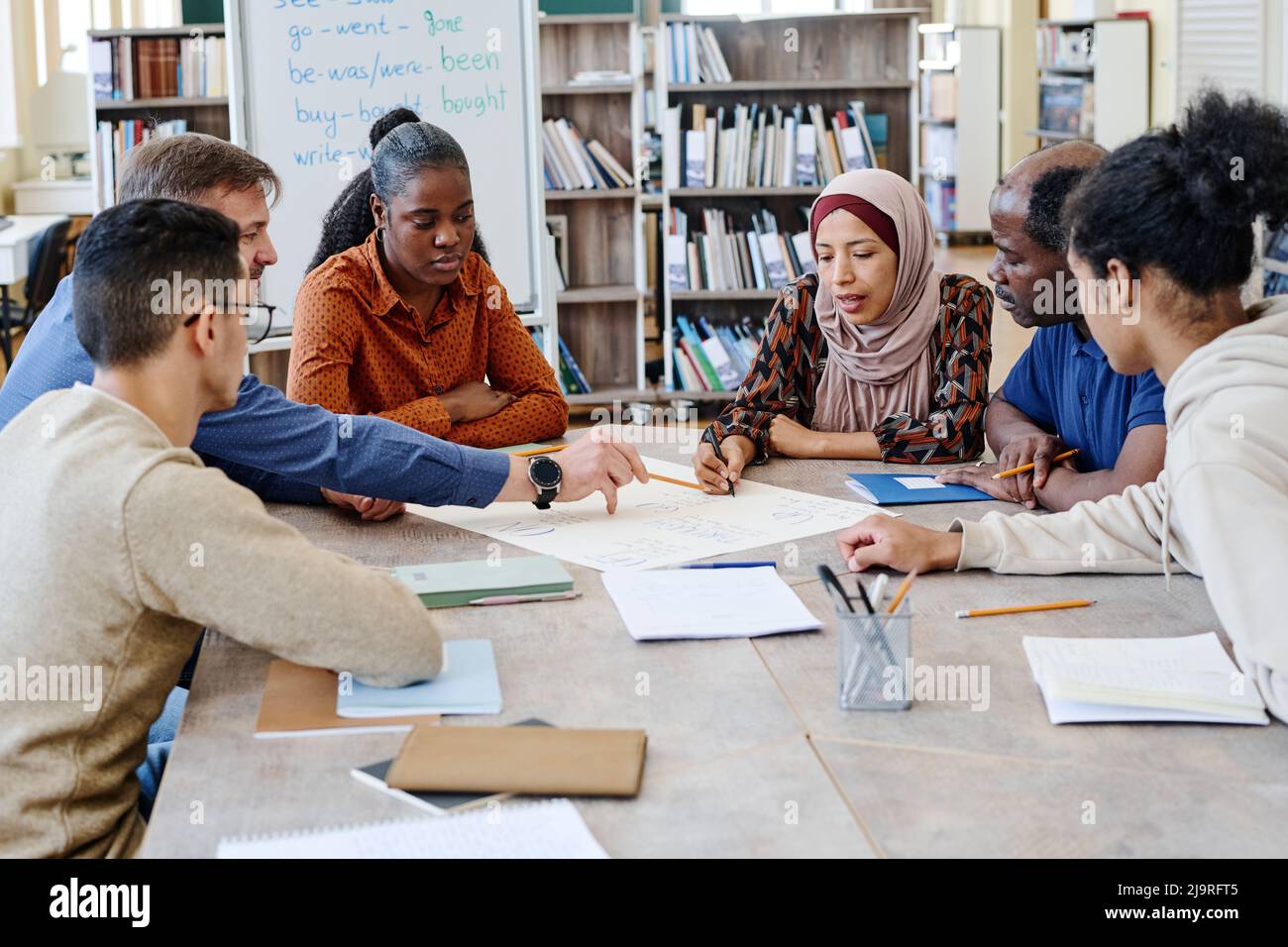 Eine Gruppe von multiethnischen Einwanderern, die an internationalen Schulstunden teilnehmen und gemeinsam an einem englischsprachigen Poster arbeiten Stockfoto