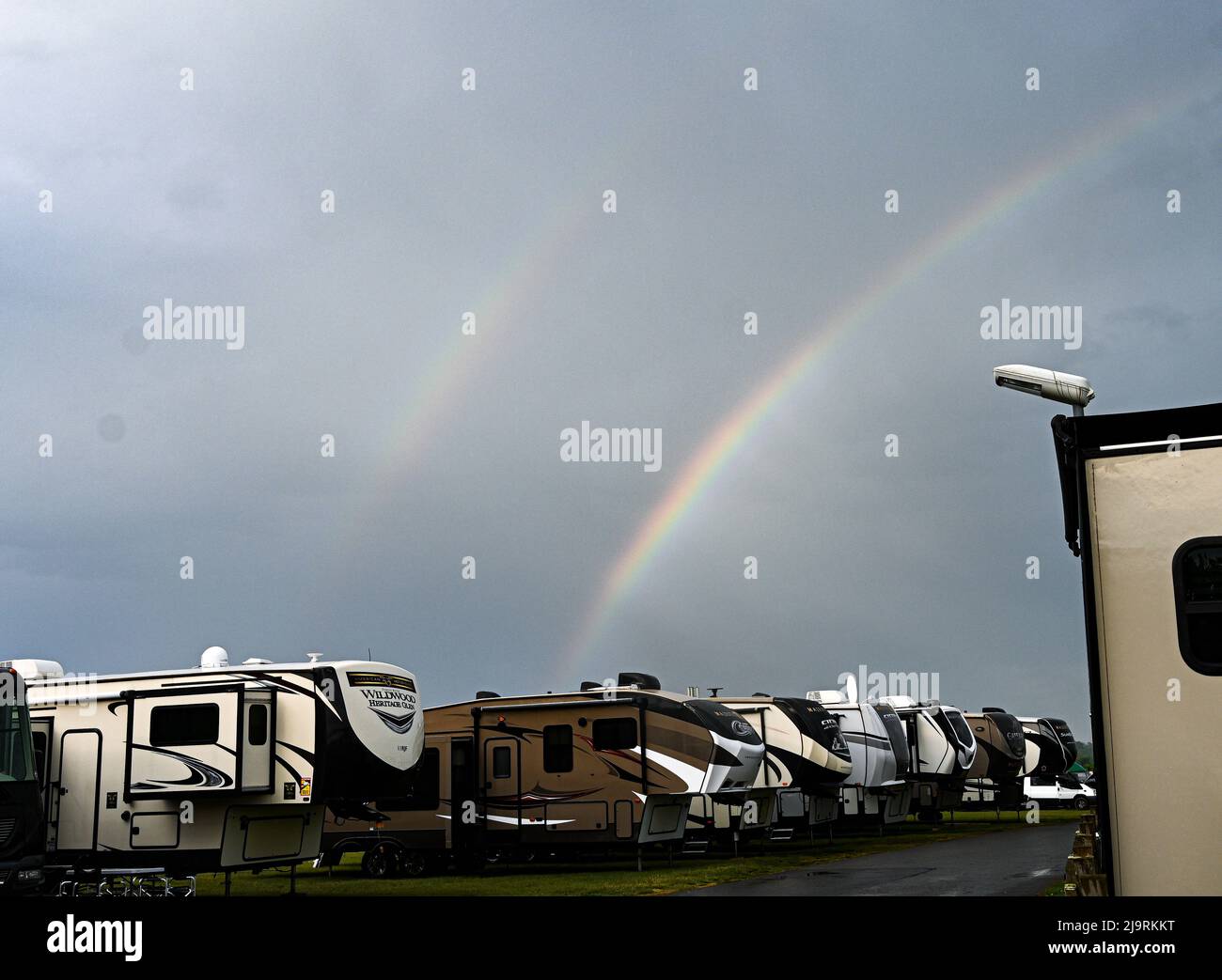 Ein doppelter Regenbogen, der auf einem dunklen launischen Himmel glitzert und über einer Reihe amerikanischer Wohnmobil-Anhänger, dem Windebago's, aufsteigt Stockfoto