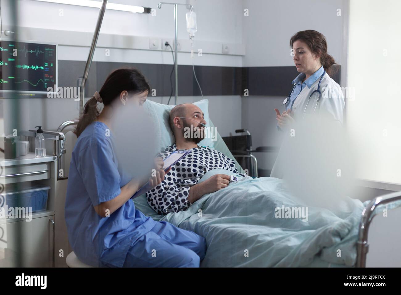 Der Arzt erklärt dem sich erholenden Mann den Behandlungsplan, während die Krankenschwester Notizen auf der Zwischenablage macht. Gesundheitsfachkraft, die ein ärztliches Rezept schreibt, während der Arzt mit dem Patienten spricht. Stockfoto