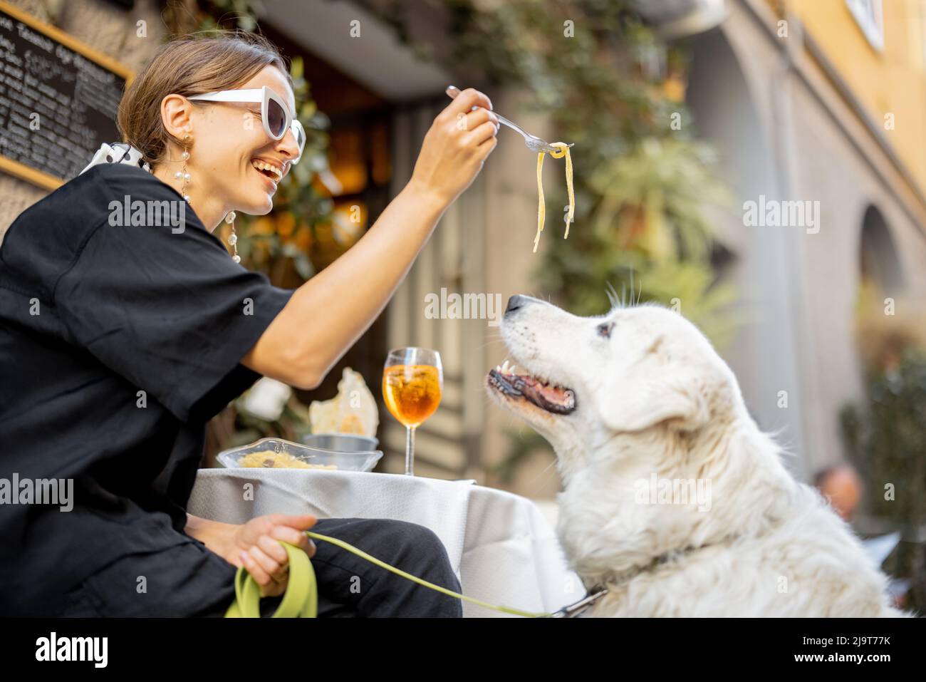 Frau, die im Restaurant mit ihrem süßen weißen Hund Pasta isst Stockfoto