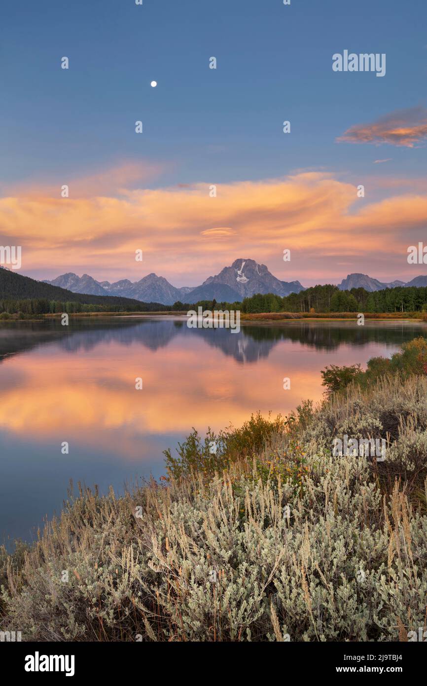Vollmond, orangefarbene Wolken am Oxbow Bend bei Sonnenaufgang, Grand Teton National Park, Wyoming. Stockfoto