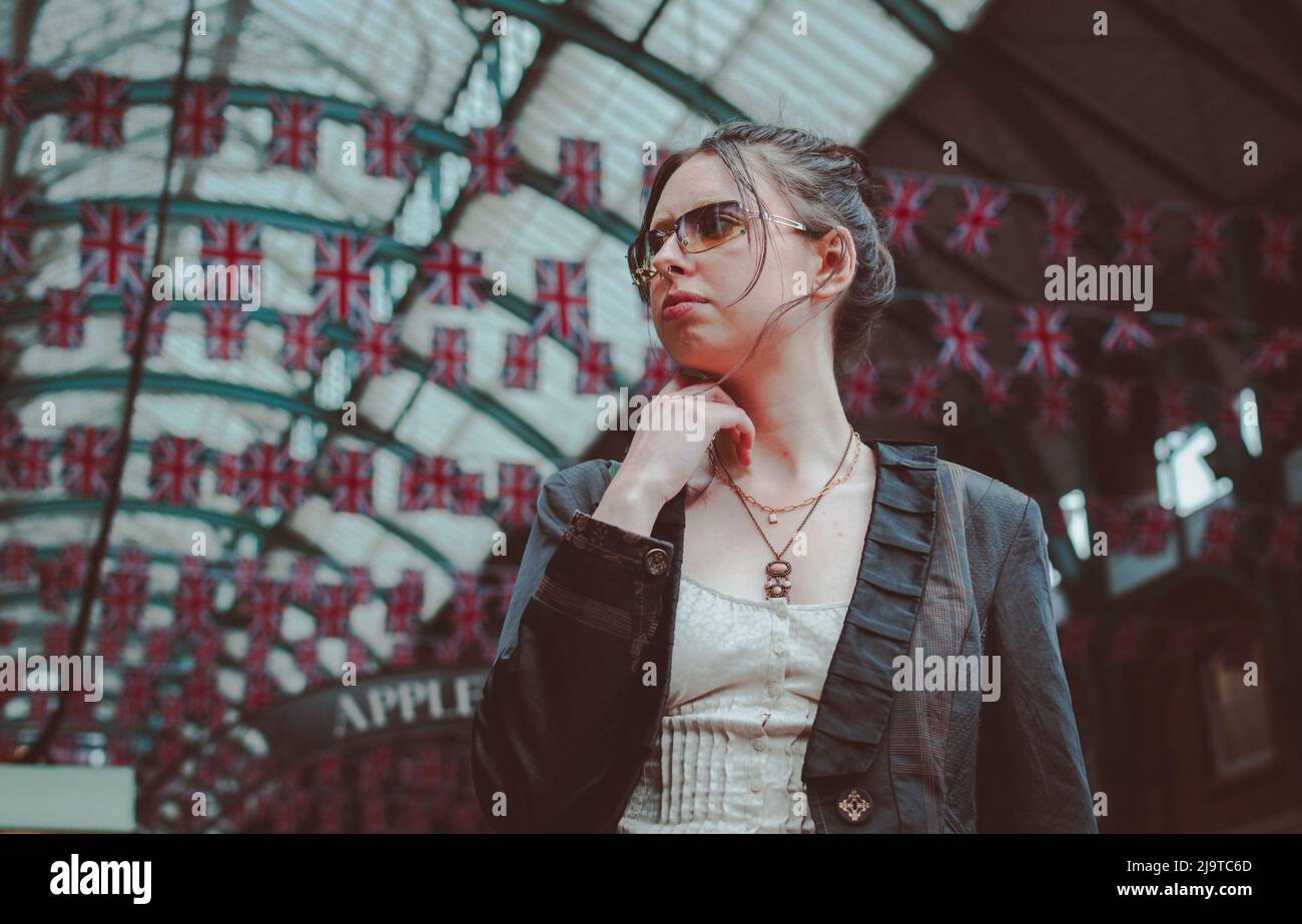 Junge Frau, die vor dem Apple Market in Covent Garden London steht und Union Jack hinter ihr fliegt. Stockfoto