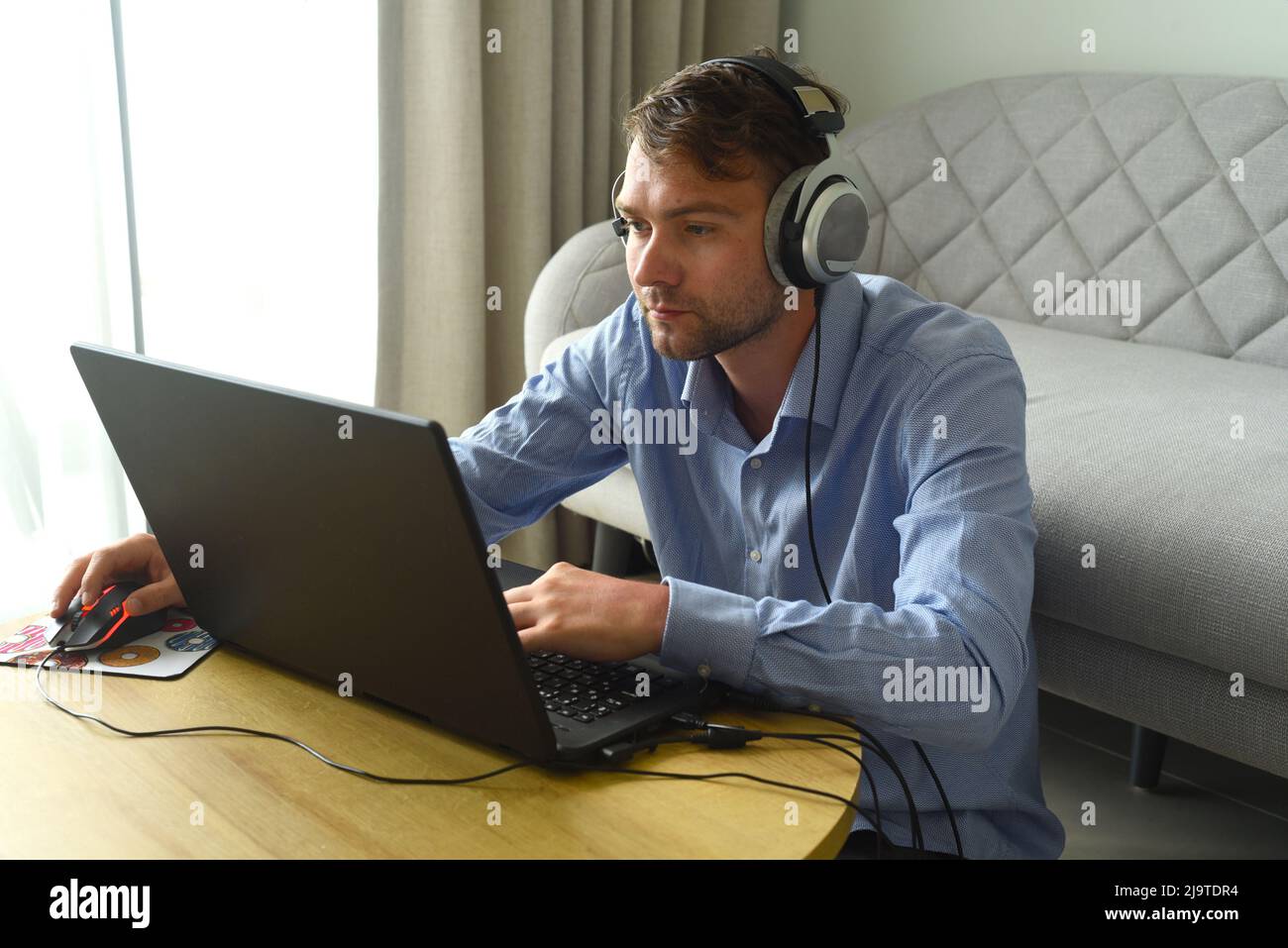 Junger Mann mit Kopfhörern, der zu Hause in einem Laptop arbeitet Stockfoto