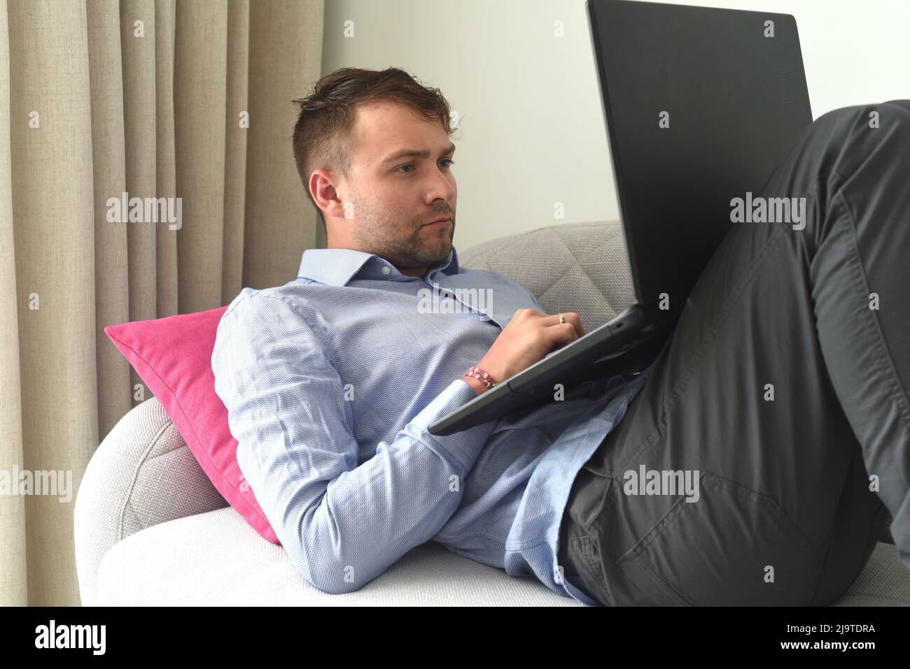 Junger freiberuflicher Mann, der von zu Hause aus mit seinem Laptop auf der Couch arbeitet Stockfoto