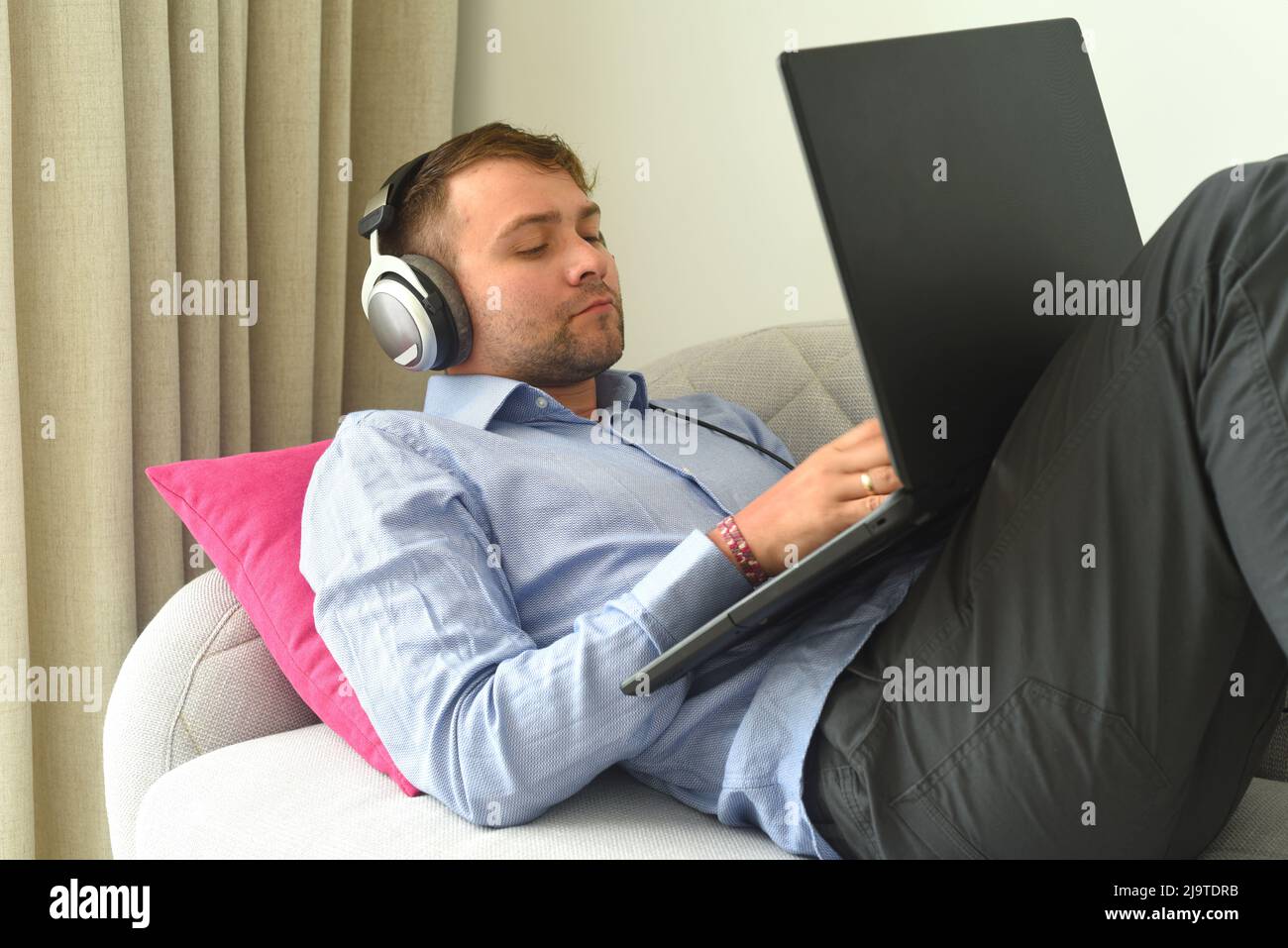 Der junge Mann schlug den Hersteller, der von zu Hause aus mit seinem Laptop auf der Couch arbeitete Stockfoto