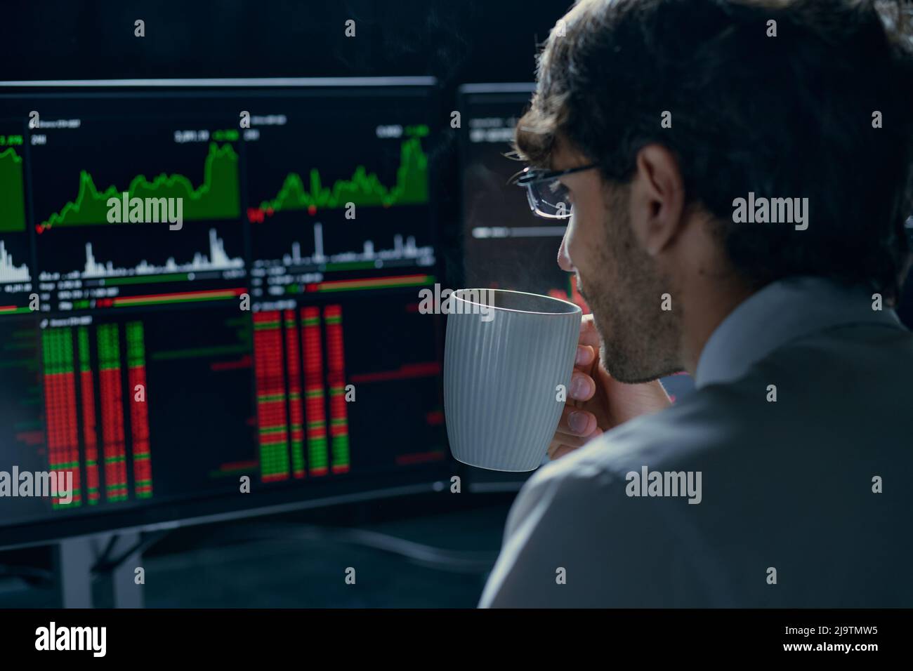 Der junge Trader mit einer Tasse Kaffee verfolgt die Daten des Kryptowährungsmarktes. Stockfoto