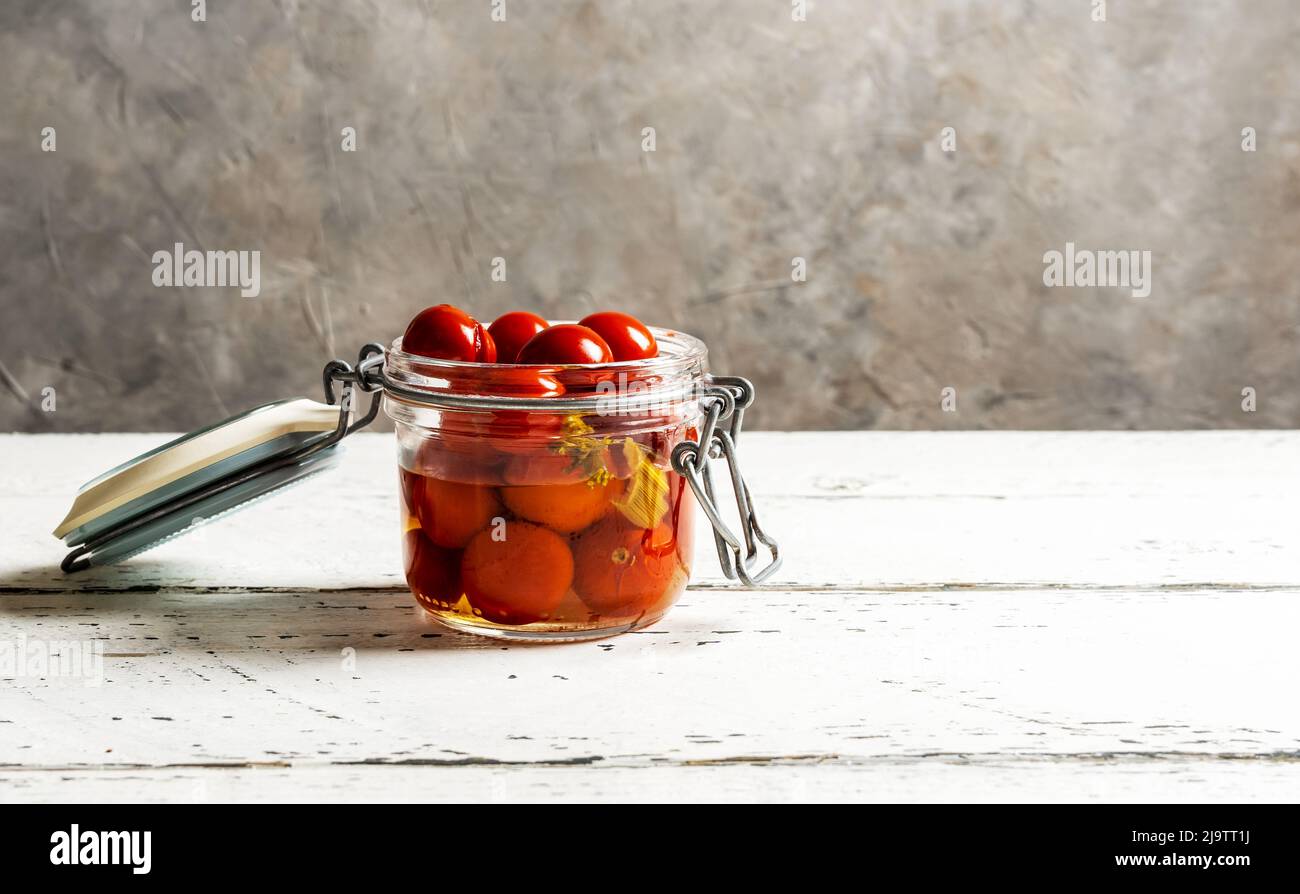 Eingelegte Tomaten in einem Glas auf weißem Holztisch mit grauem Hintergrund und Kopierraum Stockfoto