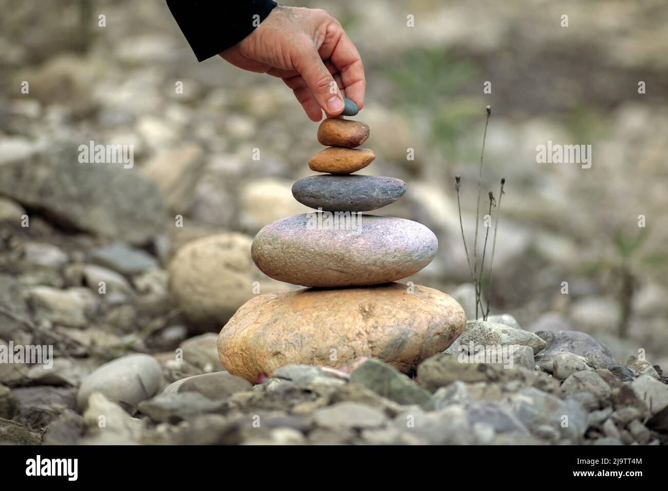 Zen-Stil Steinpyramide in einer natürlichen Umgebung mit einer Hand, die sanft legt einen Stein auf, die Frieden, Harmonie und Respekt für die Natur vermittelt Stockfoto