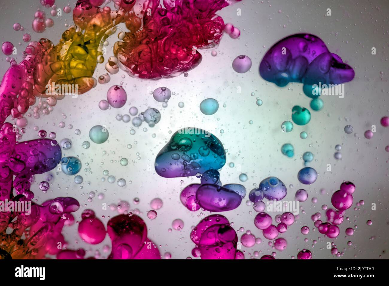 Große Wassertropfen von vielen Farben, die in einer transparenten Flüssigkeit schwimmen Stockfoto