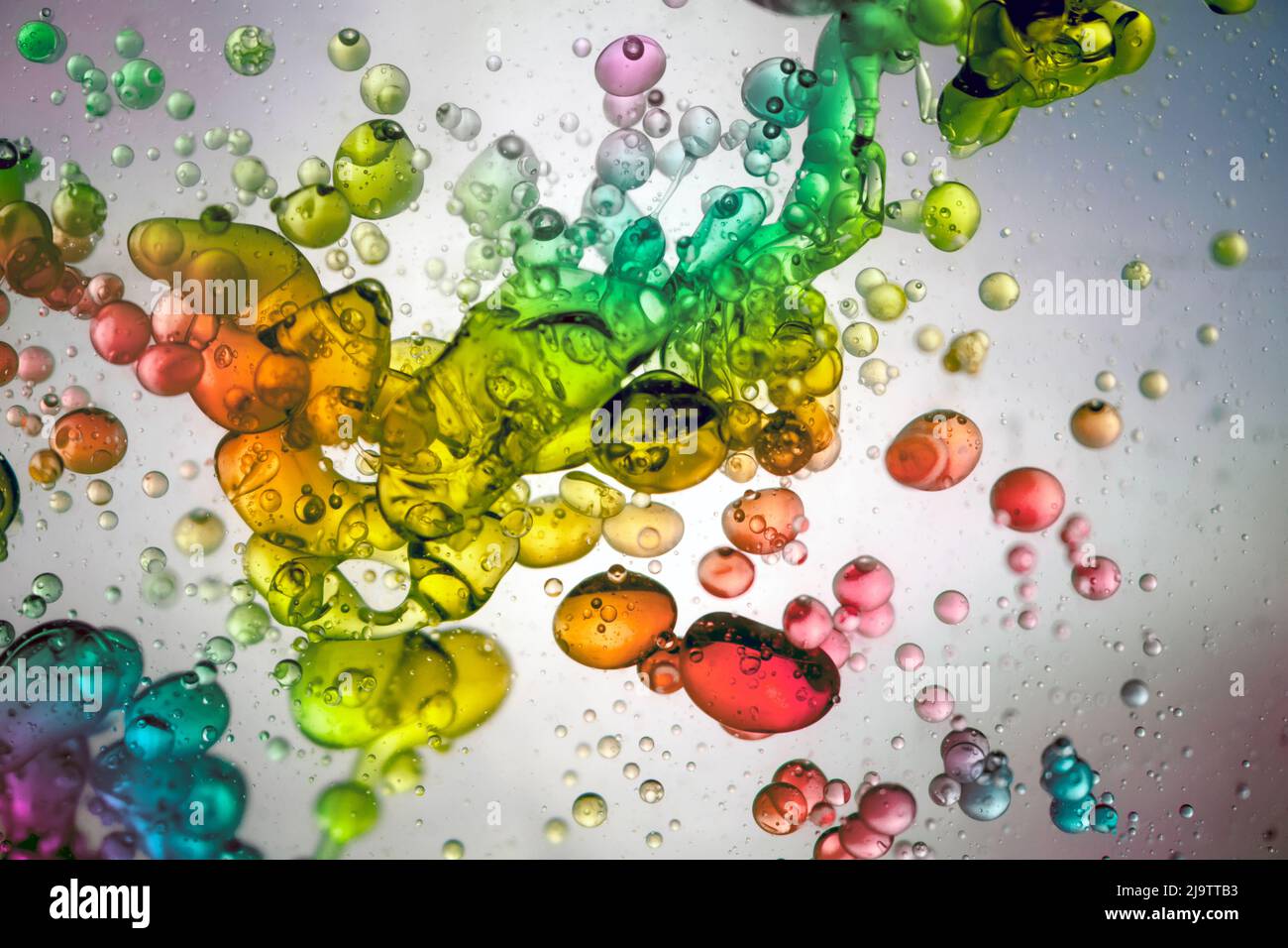 Große Wassertropfen von vielen Farben, die in einer transparenten Flüssigkeit schwimmen Stockfoto