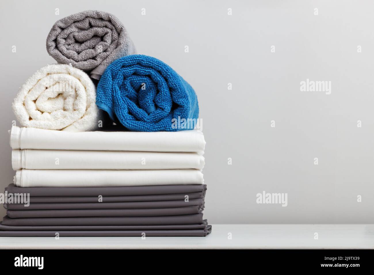 Stapel Bettwäsche, Bettwäsche, zusammengerollte Frottee-Handtücher auf dem Tisch Stockfoto