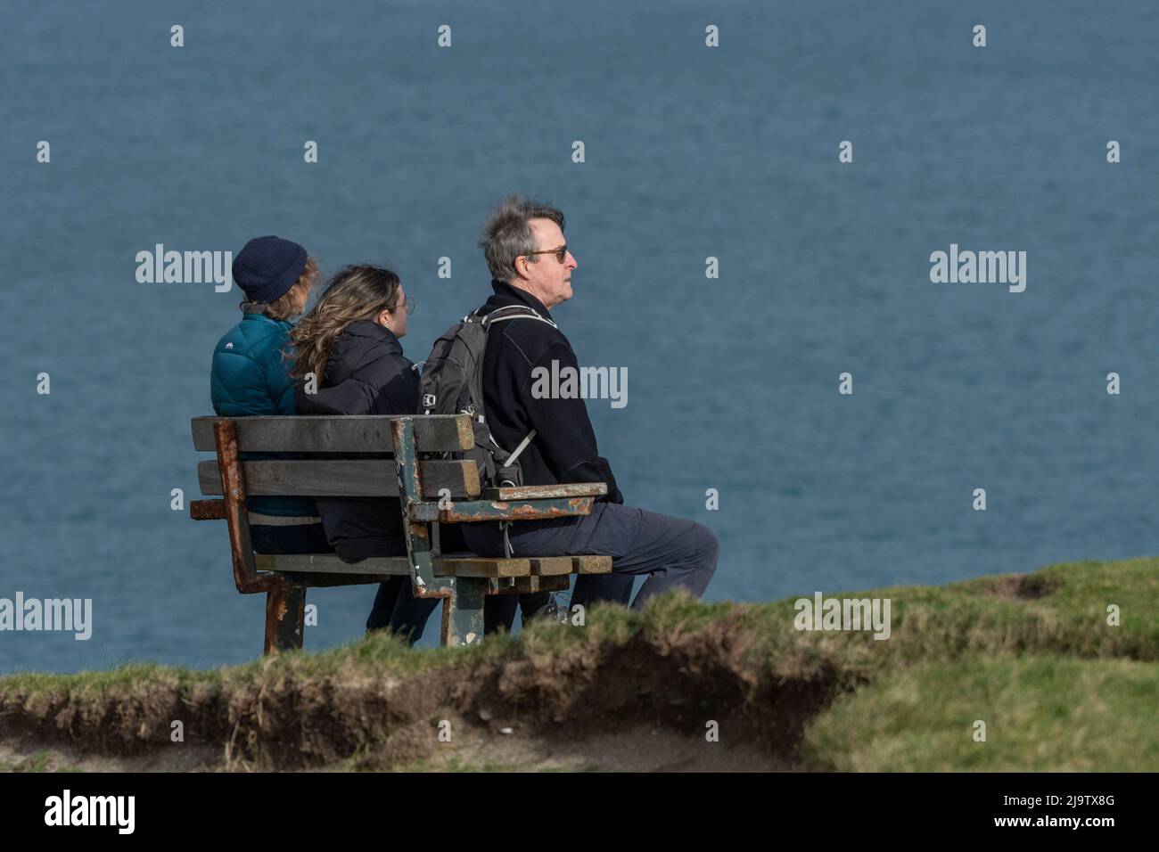 Eine Familie, die auf einer Bank mit Blick auf das Meer in Newquay in Cornwall im Vereinigten Königreich sitzt. Stockfoto