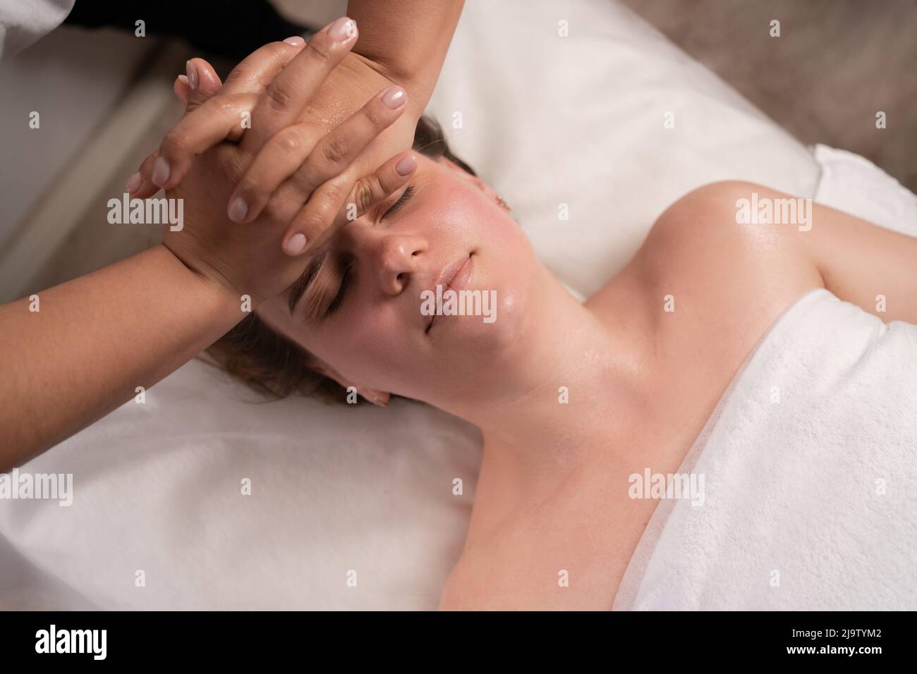 Entspannte Frau, die in einem luxuriösen Spa-Resort auf dem Spa liegt, um sich von einem Masseur eine Gesichtsmassage zu gönnen. Wellness, Stressabbau und Verjüngung Stockfoto