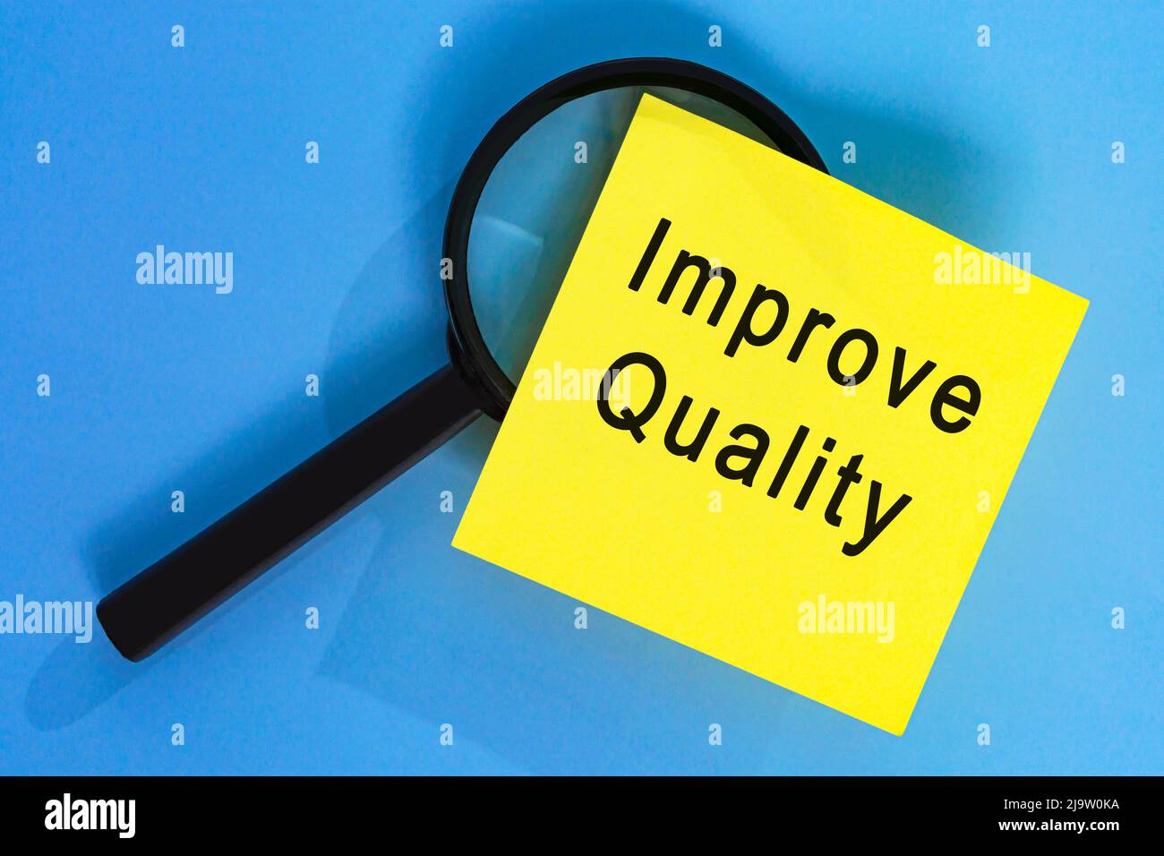 Verbessern Sie die Qualität auf Klebenotizen mit Vergrößerungsglas vor blauem Hintergrund. Geschäftskonzept. Stockfoto