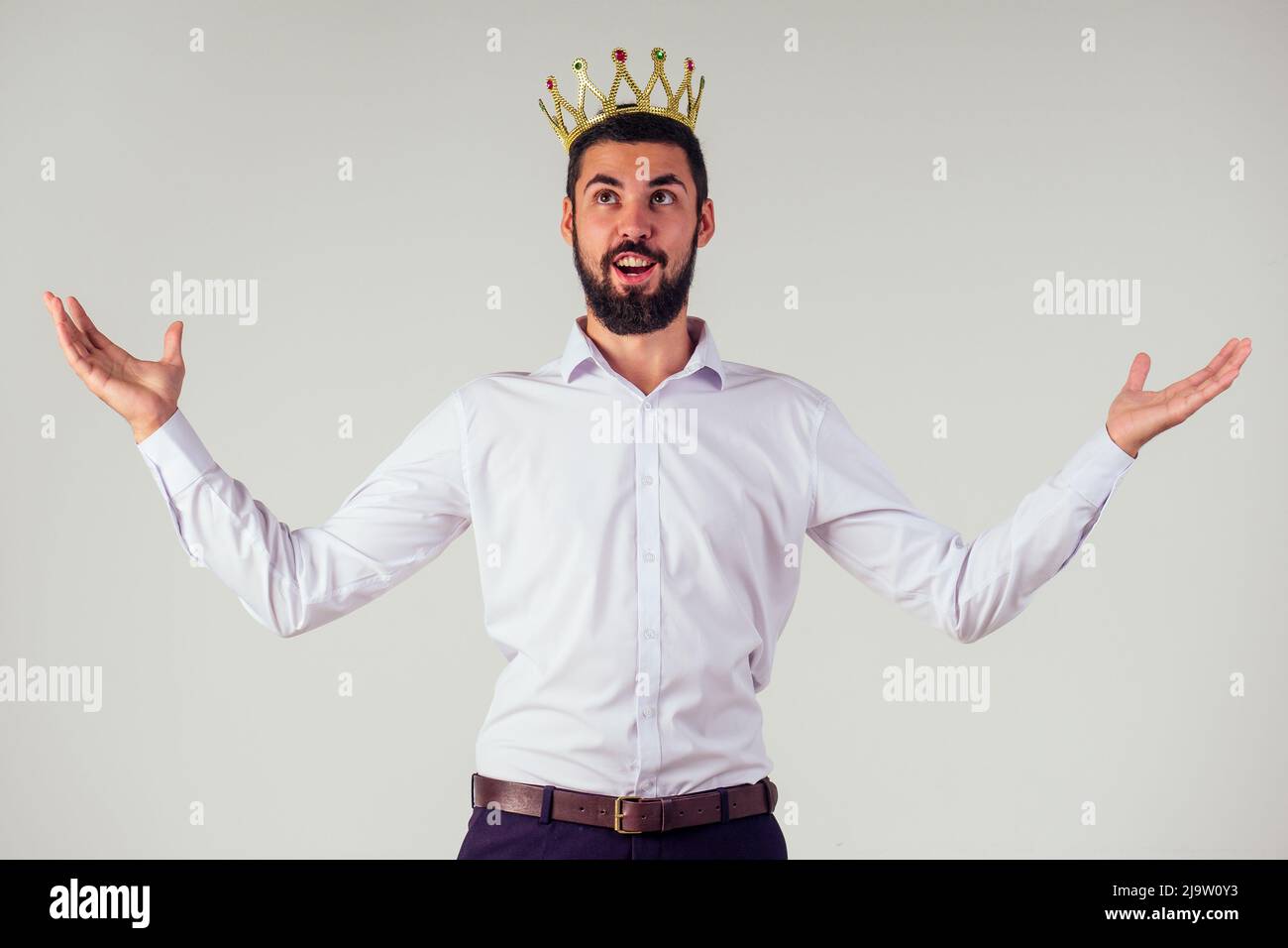 Porträt eines lächelnden bärtigen Geschäftsmanns mit einer goldenen Krone auf dem Kopf auf weißem Hintergrund, aufgenommen im Studio Stockfoto