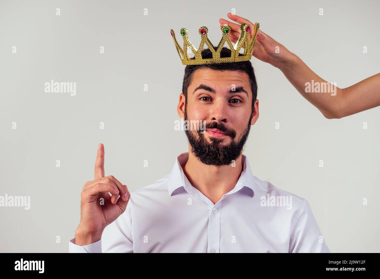 Porträt eines lächelnden bärtigen Geschäftsmanns mit einer goldenen Krone auf dem Kopf auf weißem Hintergrund, aufgenommen im Studio Stockfoto