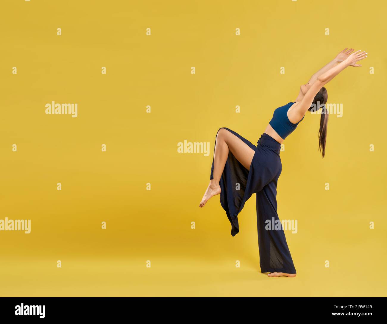 Moderne Tänzerin trägt weite Schlitze Hosen, Durchführung Tanz Posen und Bewegungen im Freien. Yogi-Mädchen, das Yoga praktiziert, mit Kopierraum, isoliert auf orangefarbenem Studiohintergrund. Konzept des Lebensstils. Stockfoto