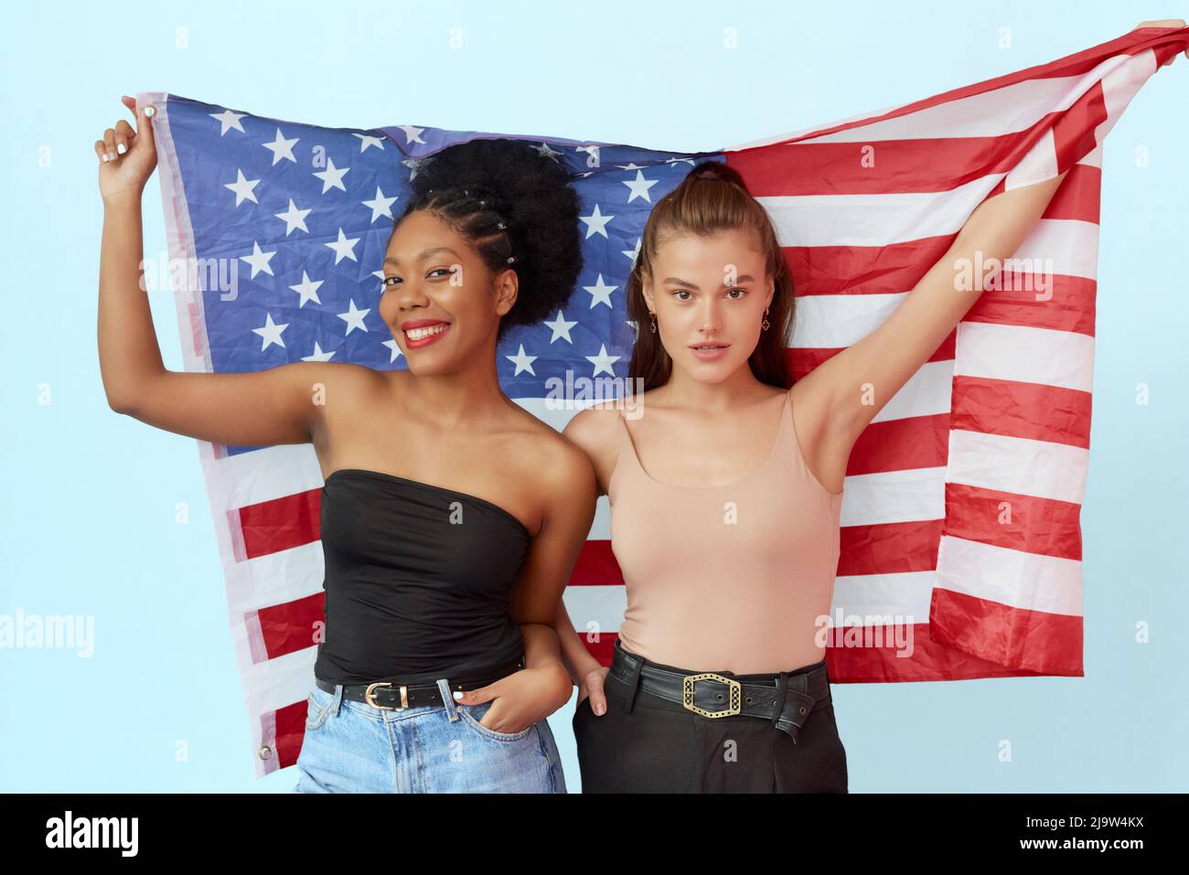 afroamerikanische Frau und Kaukasierin mit US-Flagge im Studio auf blauem Hintergrund. Das Konzept der Einheit der verschiedenen Nationen und unabhängig Stockfoto