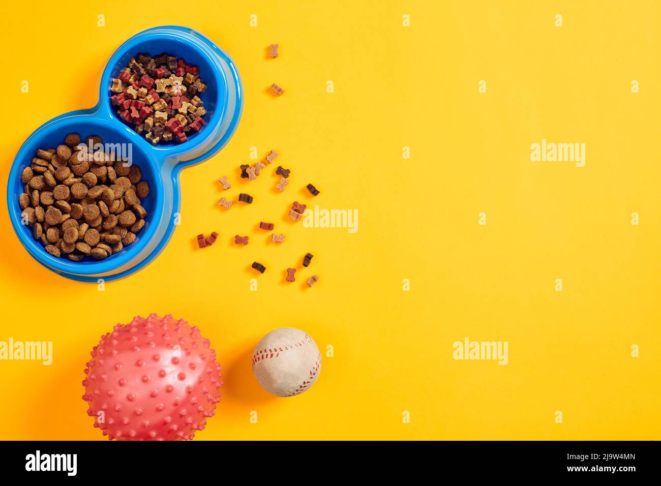 Trockenes Tierfutter in Schüssel mit einem Ball auf gelbem Hintergrund Draufsicht Stockfoto
