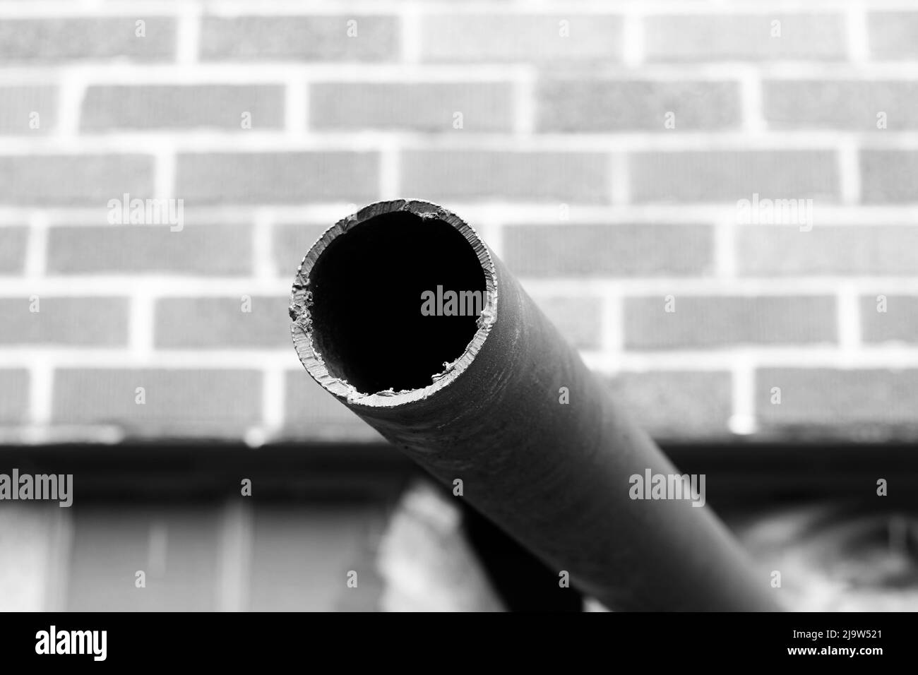 Altes verrosttes Rohr, das schwarz-weiß aus der Wand ragt. Stockfoto