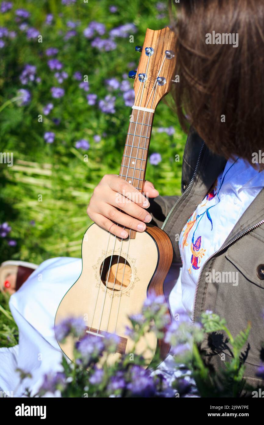 Ukulele Musikinstrument in weiblicher Hand. Frau, die im Frühling in Blumen sitzt Stockfoto