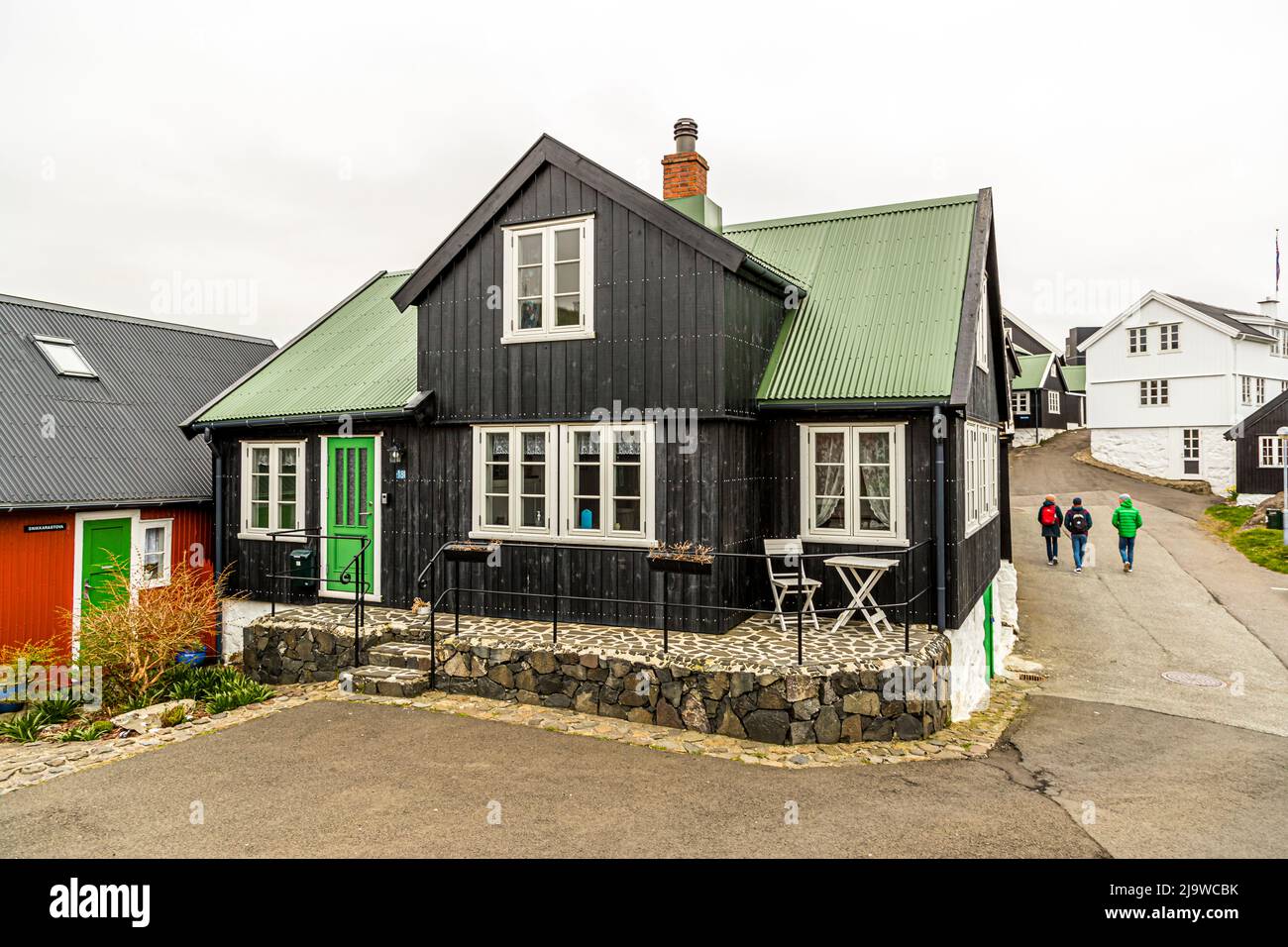 Drei Passanten gehen die Gongin hinunter, eine Gasse in der historischen Altstadt von Tórshavn, der Hauptstadt der Färöer-Inseln. Mit Torf bedeckte Holzhäuser, schwarz und grün gestrichen, säumen die abschüssige Straße, mit einem roten Haus auf der linken Seite. Der Name Tórshavn bedeutet „Thors Hafen“ nach dem nordischen Gott Thor. Stockfoto