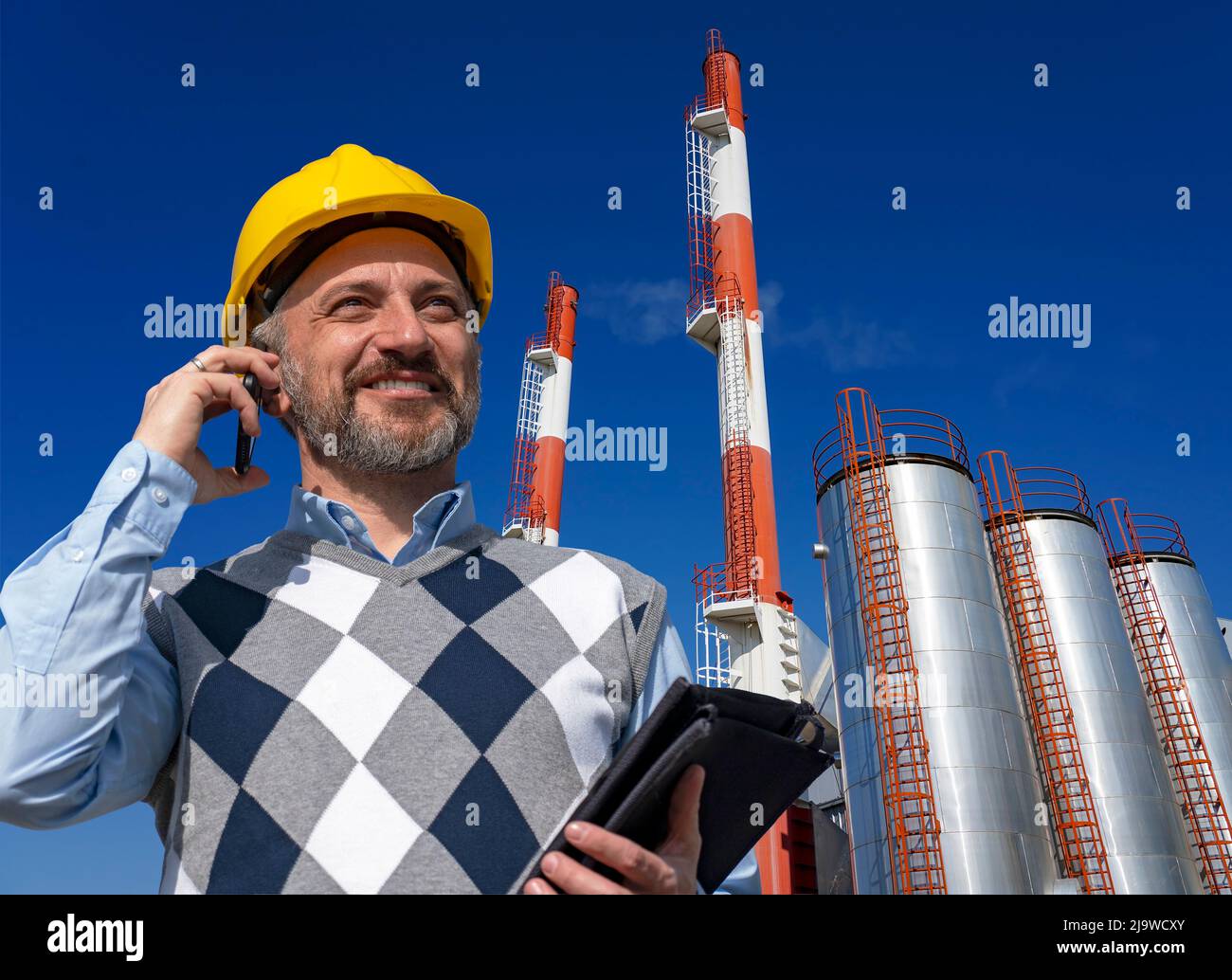 Porträt eines lächelnden Produktionsleiters mit Smartphone in der Fernwärmeanlage. Stockfoto