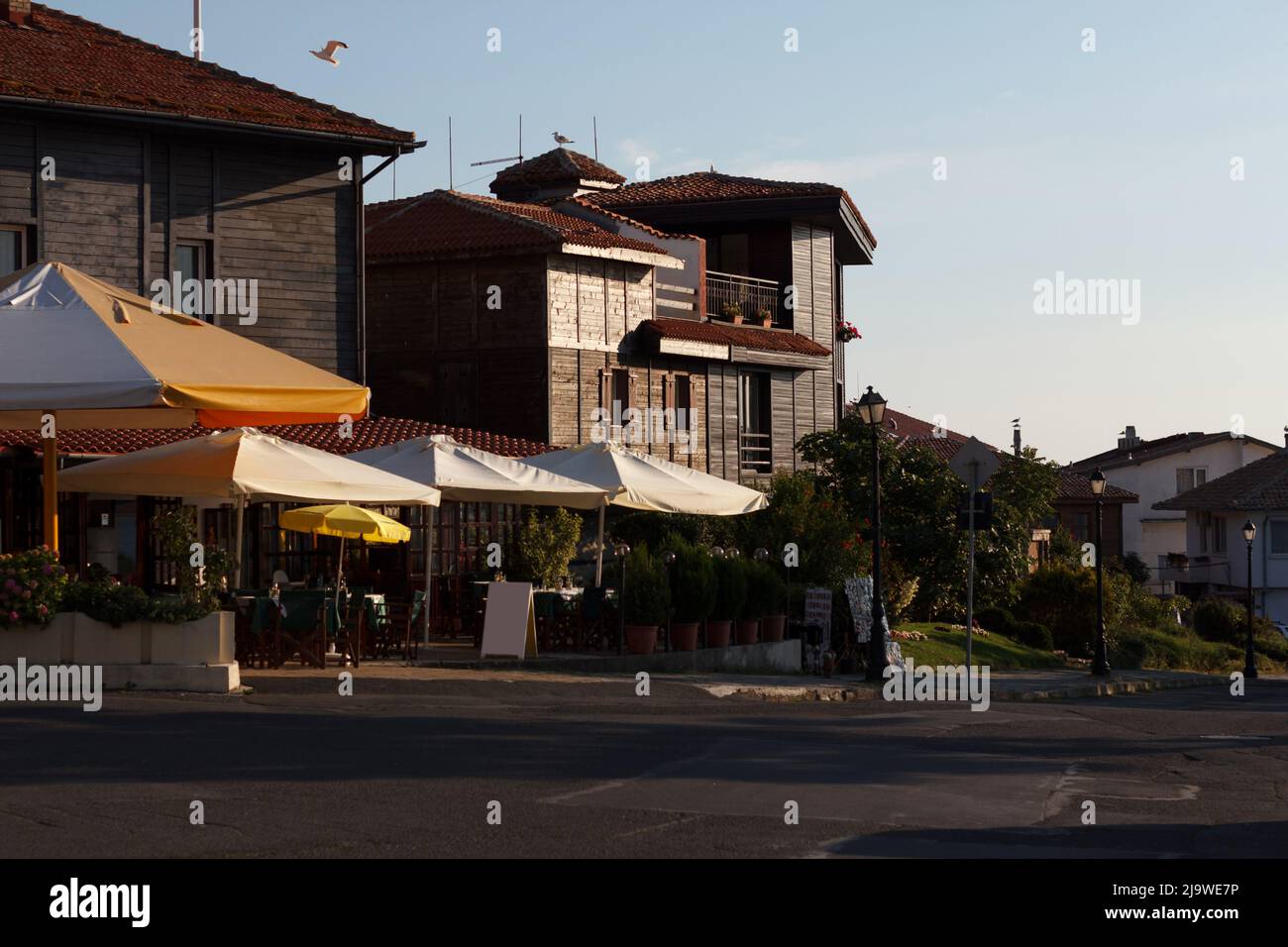 Reisen Sie in Bulgarien, Sommerterrasse für Touristen, Café mit Sonnenschirmen, neben hölzernen 2-3-stöckigen Gebäuden Stockfoto