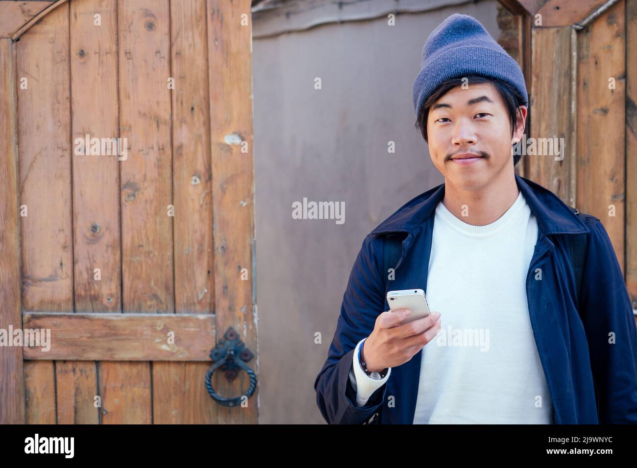 Netter Tourist aus Korea mit einem Rucksack, der in das Telefon schaut Stockfoto