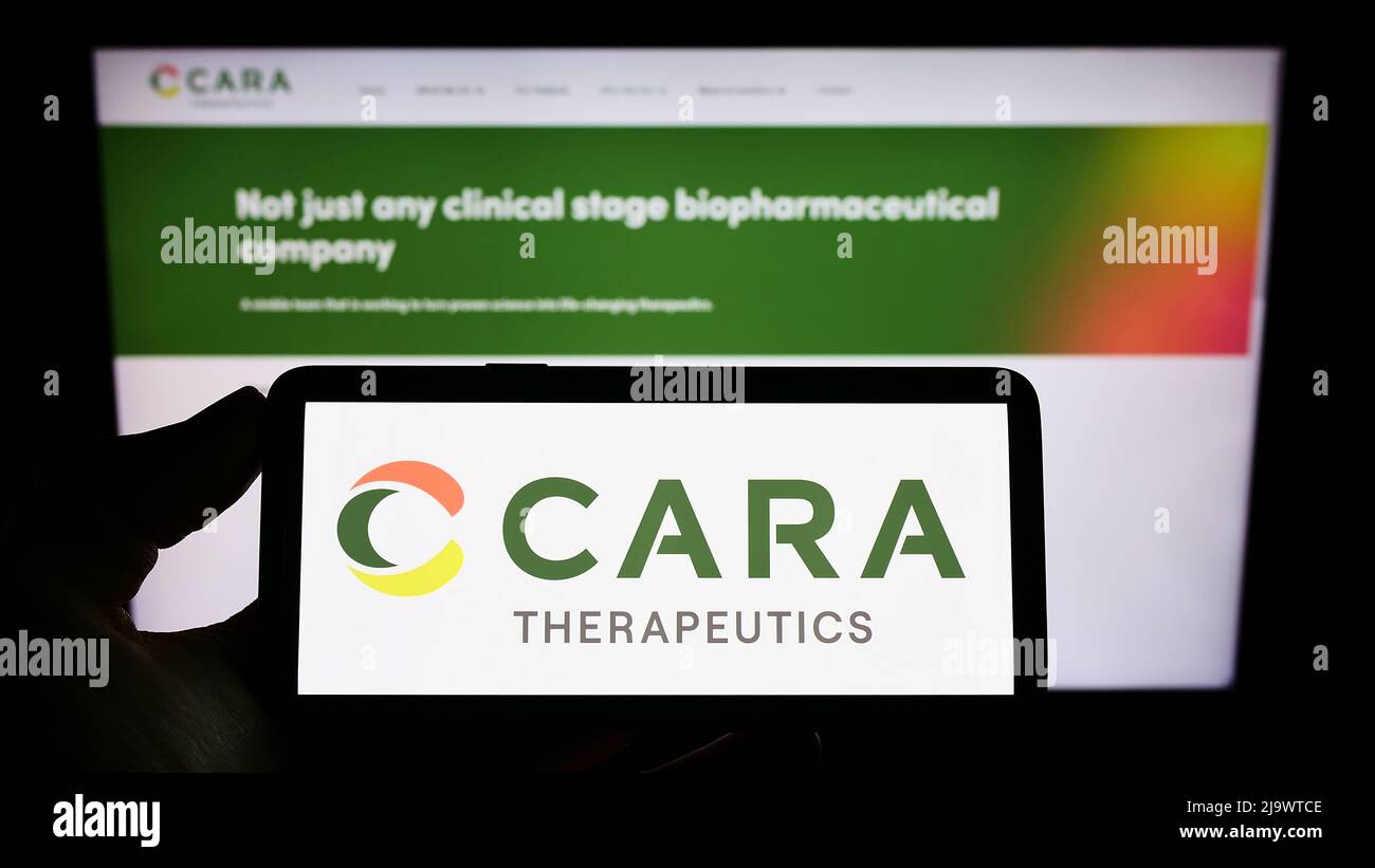 Person mit Mobiltelefon und Logo des amerikanischen Biotech-Unternehmens Cara Therapeutics Inc. Auf dem Bildschirm vor der Webseite. Konzentrieren Sie sich auf die Telefonanzeige. Stockfoto