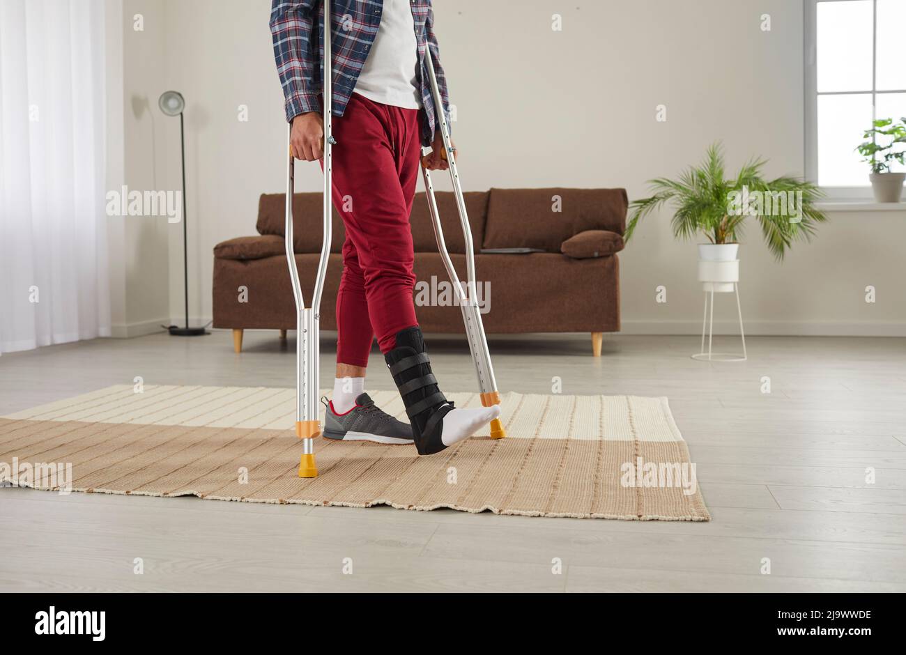 Gebrochenes Bein des Mannes in schwarzem Spezialverband, um Verletzungen durch Verstauchungen des Knöchels zu Hause zu behandeln. Stockfoto