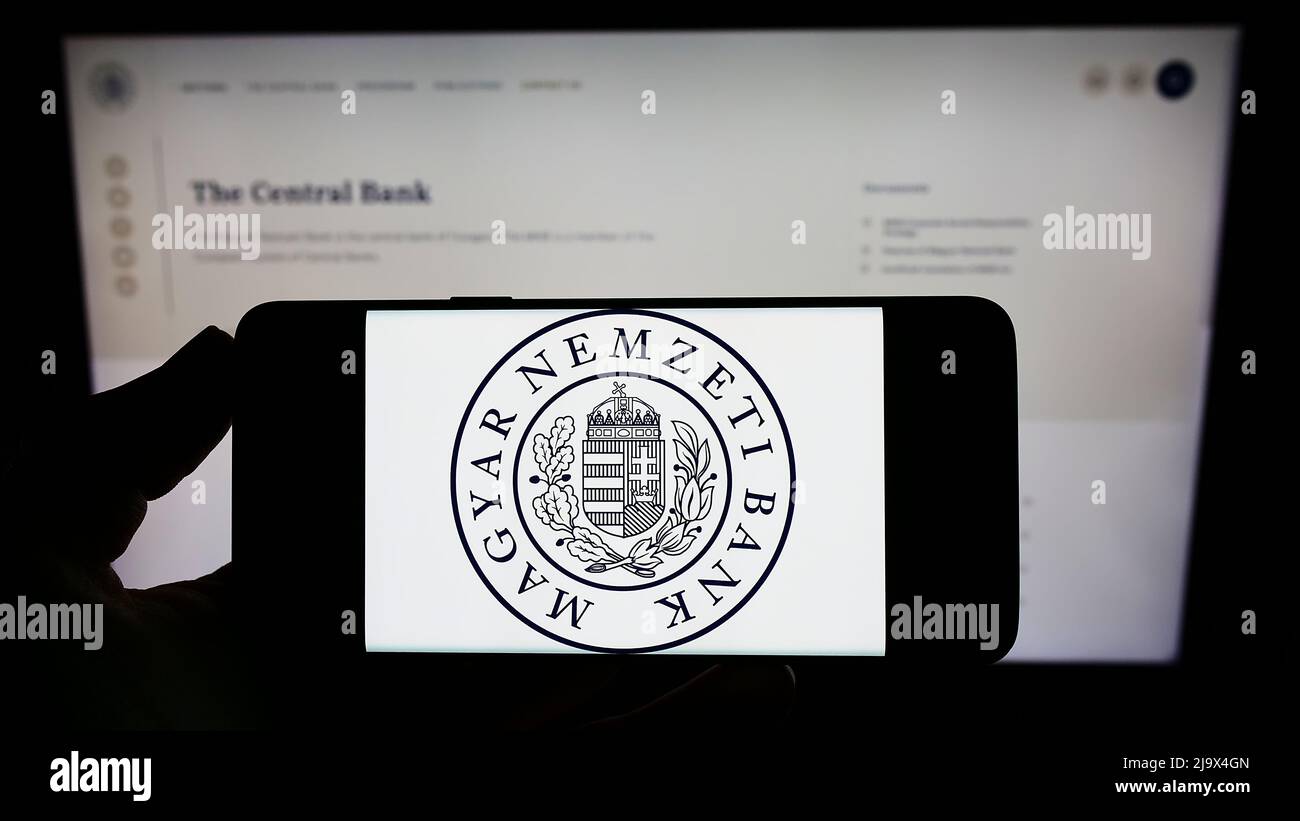 Person, die das Smartphone mit dem Logo der Ungarischen Nationalbank (Magyar Nemzeti Bank, MNB) auf dem Bildschirm vor der Website hält. Konzentrieren Sie sich auf die Telefonanzeige. Stockfoto