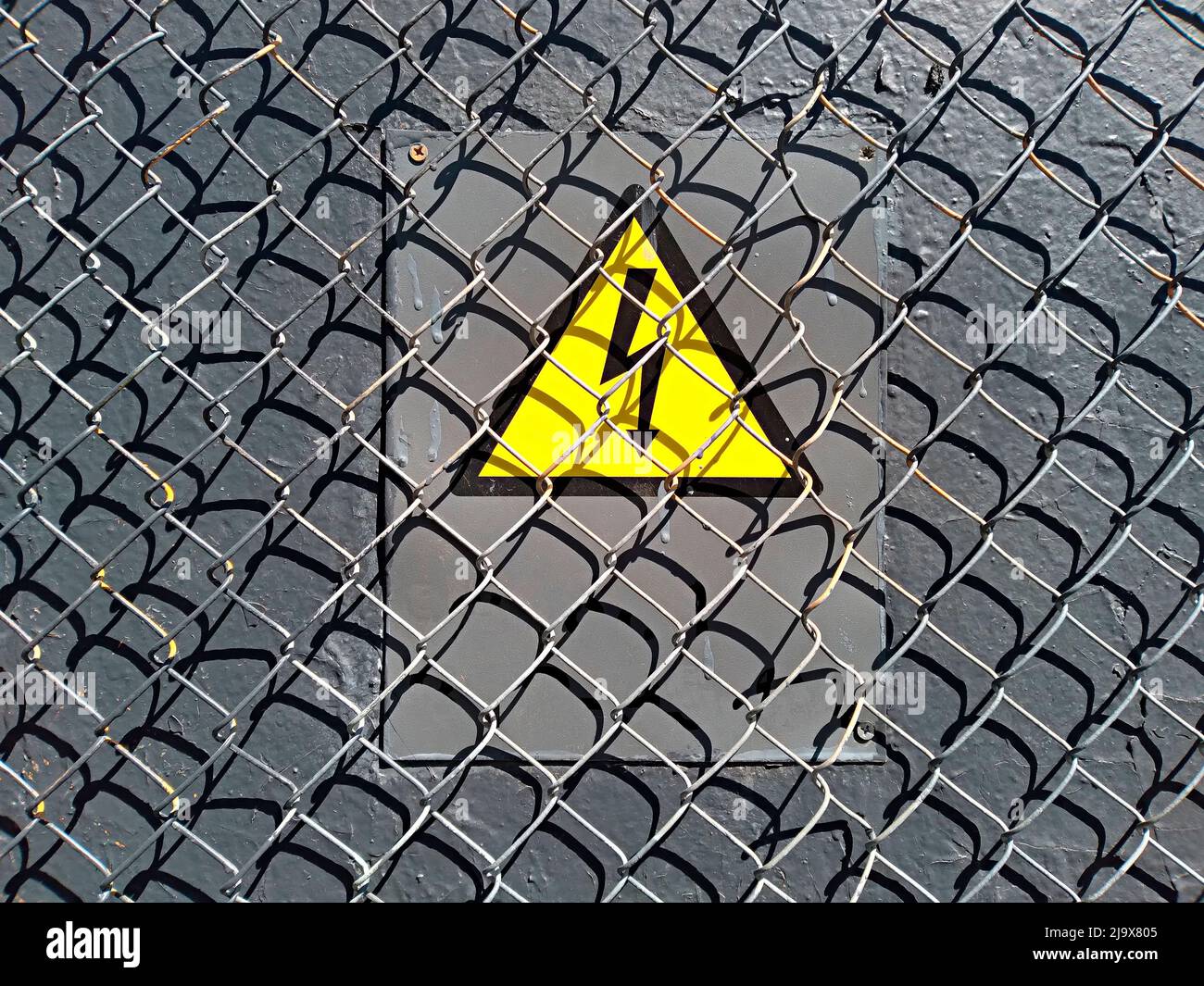 Schild für elektrische Gefahren auf einem Umspannwerk hinter einem Metallzaun aus Drahtgeflecht, Sanktionen, Einschränkungen Stockfoto
