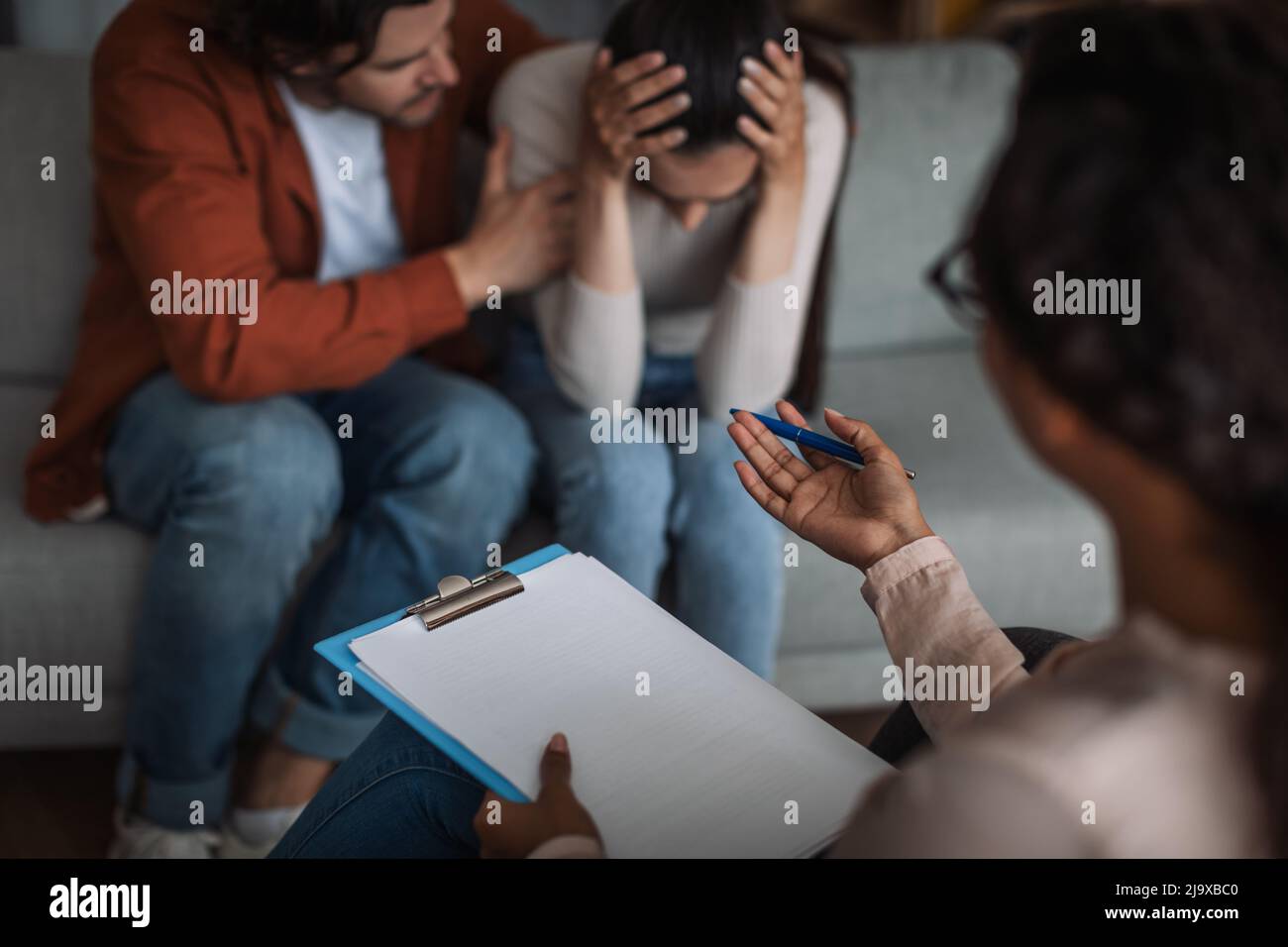 Unglücklicher junger europäischer Mann beruhigt weinende Frau und spricht mit dem Psychologen im Klinikinnern Stockfoto