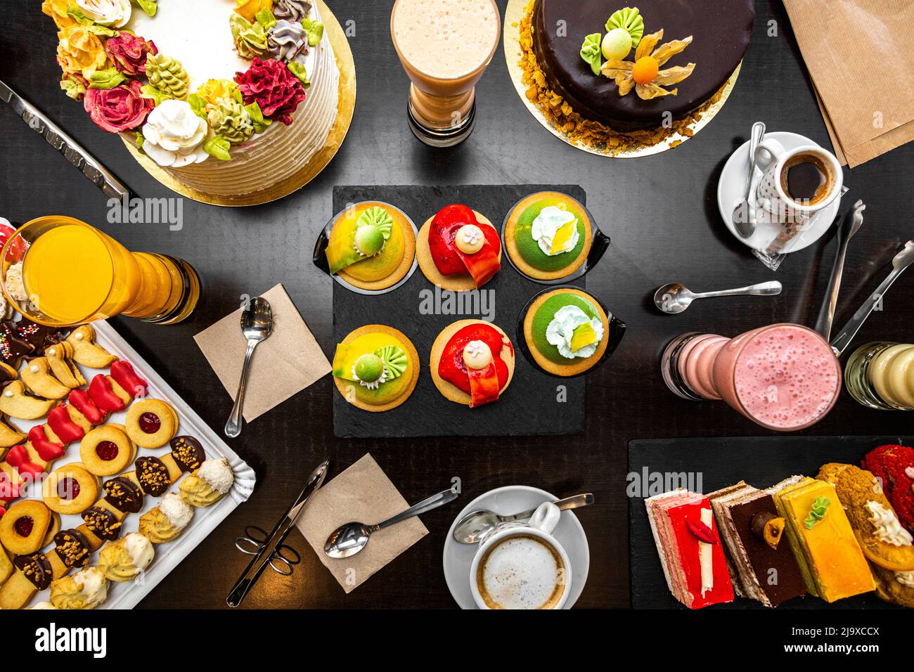 Dessert und Kuchen auf einem schwarzen Tisch, Cremeschokolade, Puderzucker, Buttercroissants, Orangensaft, Teekuchen, süße Schnecken. Stockfoto
