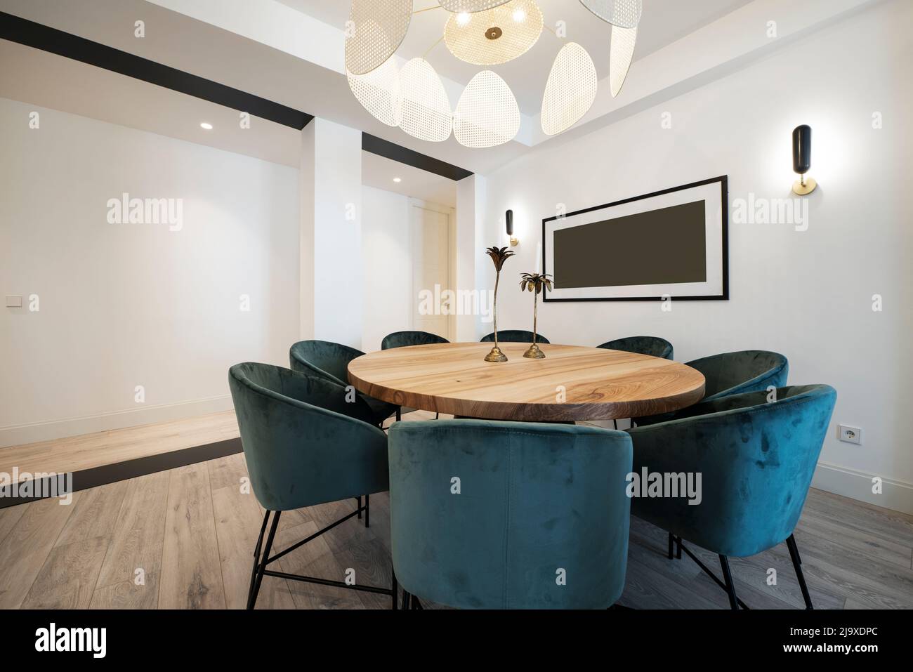 Runder Esstisch mit Rohholzlack, umgeben von blauen gepolsterten Samtsesseln unter einer Designer-Lampe Stockfoto